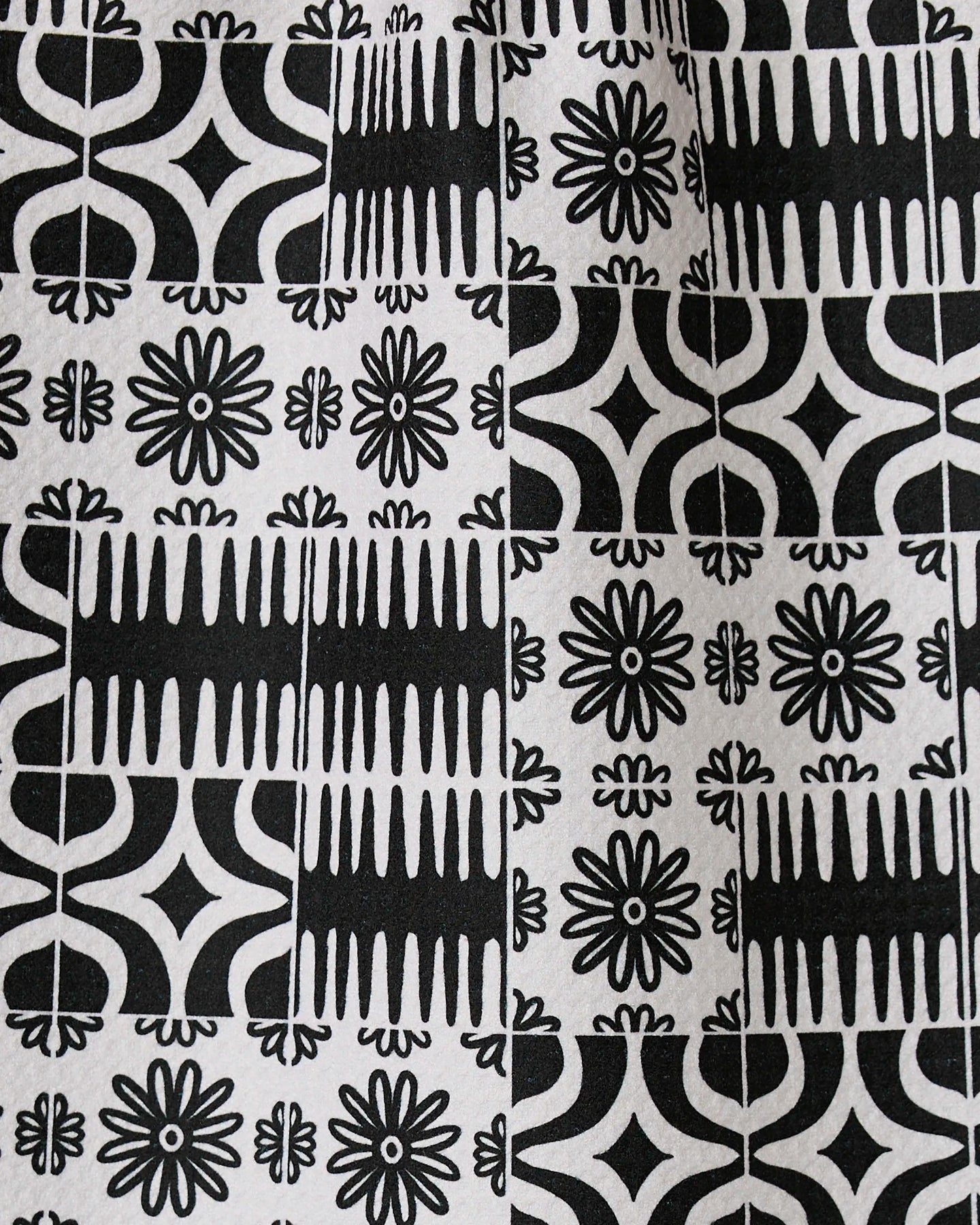 Bohemian Mosaic by GEOMETRY features black and white tiles with alternating geometric and floral patterns, including starbursts, lines, and curves. Crafted from recycled materials, these designs repeat in a grid for a bold look.