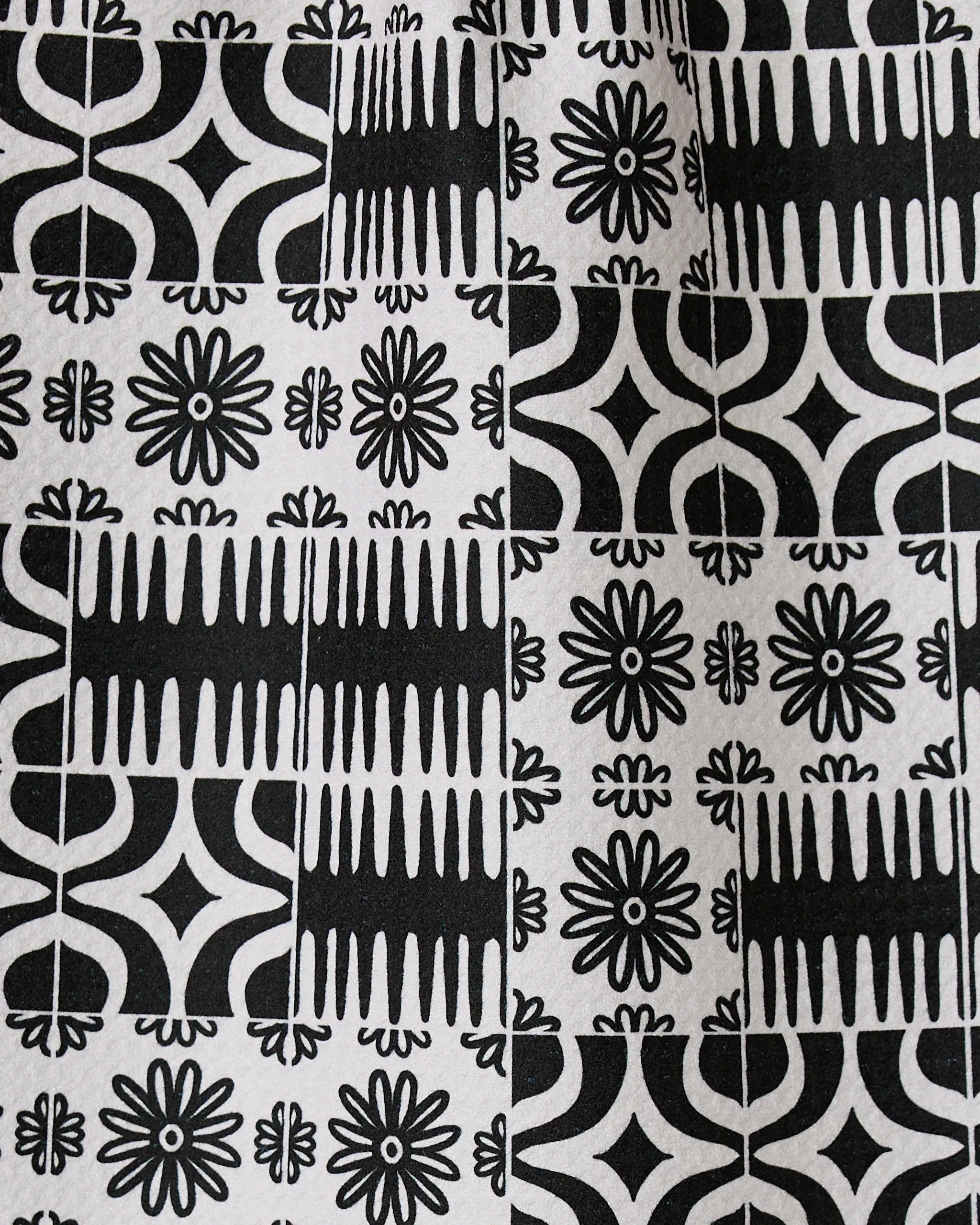 Bohemian Mosaic by GEOMETRY features black and white tiles with alternating geometric and floral patterns, including starbursts, lines, and curves. Crafted from recycled materials, these designs repeat in a grid for a bold look.
