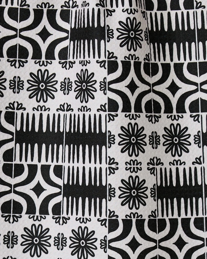 Bohemian Mosaic by GEOMETRY features black and white tiles with alternating geometric and floral patterns, including starbursts, lines, and curves. Crafted from recycled materials, these designs repeat in a grid for a bold look.