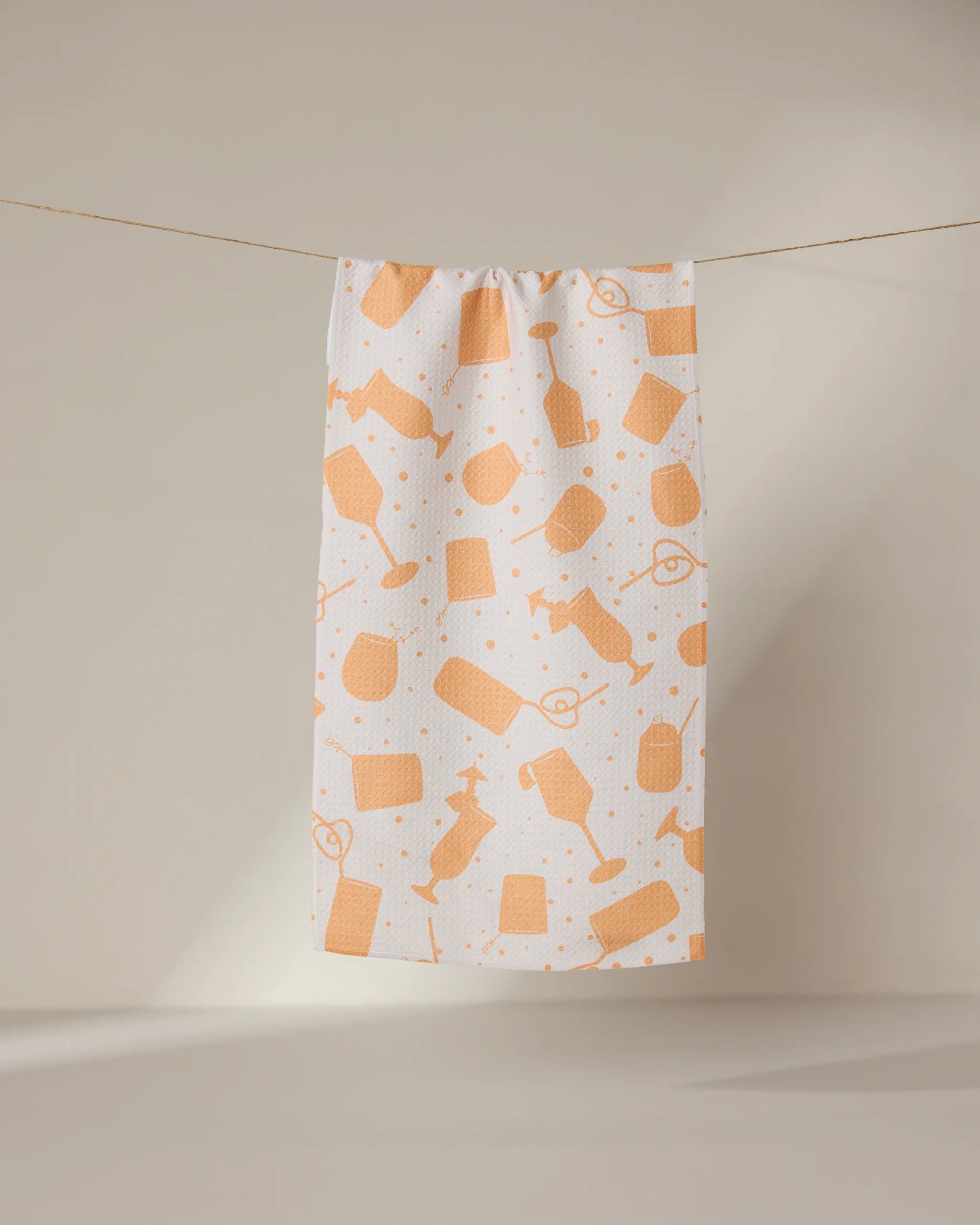 The GEOMETRY Bach Brunch bar towel is white, made from recycled materials, and features an orange hairdressing tool pattern. It hangs on a clothesline against a neutral background.