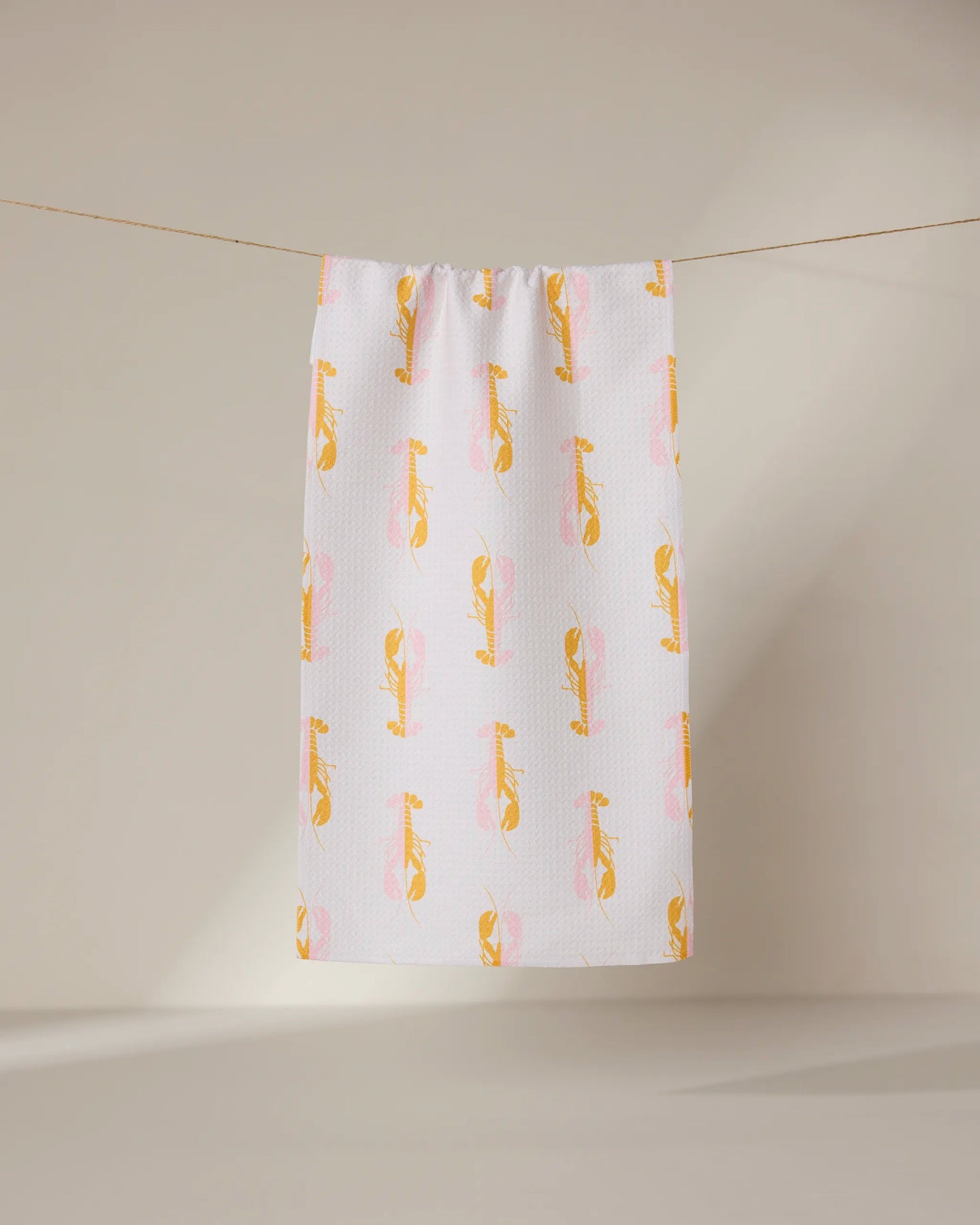 The GEOMETRY Lobster Love towel, ultra-absorbent and white with a pattern of yellow and pink cartoon cheetahs, hangs on a clothesline against a plain, light background.