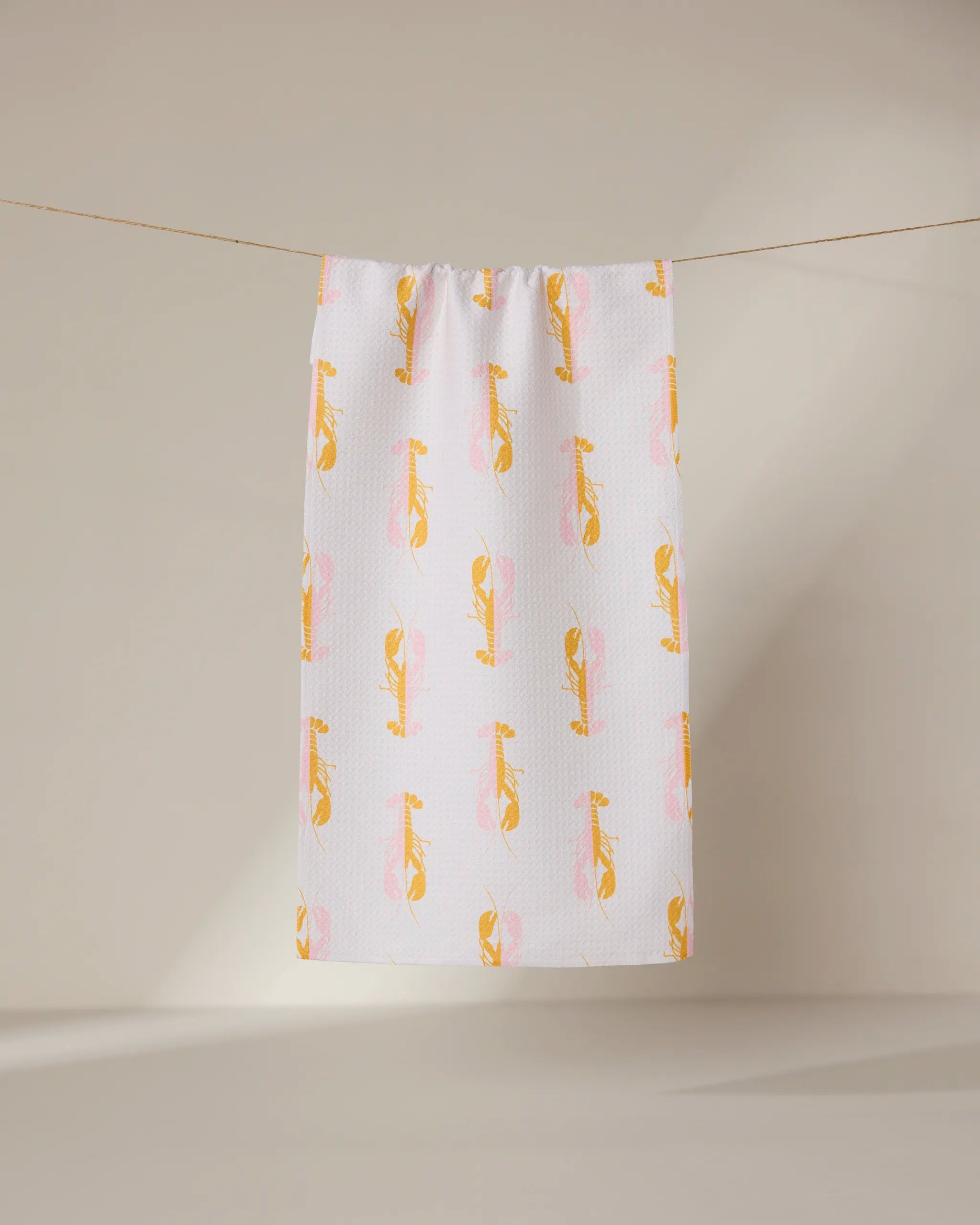 The GEOMETRY Lobster Love towel, ultra-absorbent and white with a pattern of yellow and pink cartoon cheetahs, hangs on a clothesline against a plain, light background.
