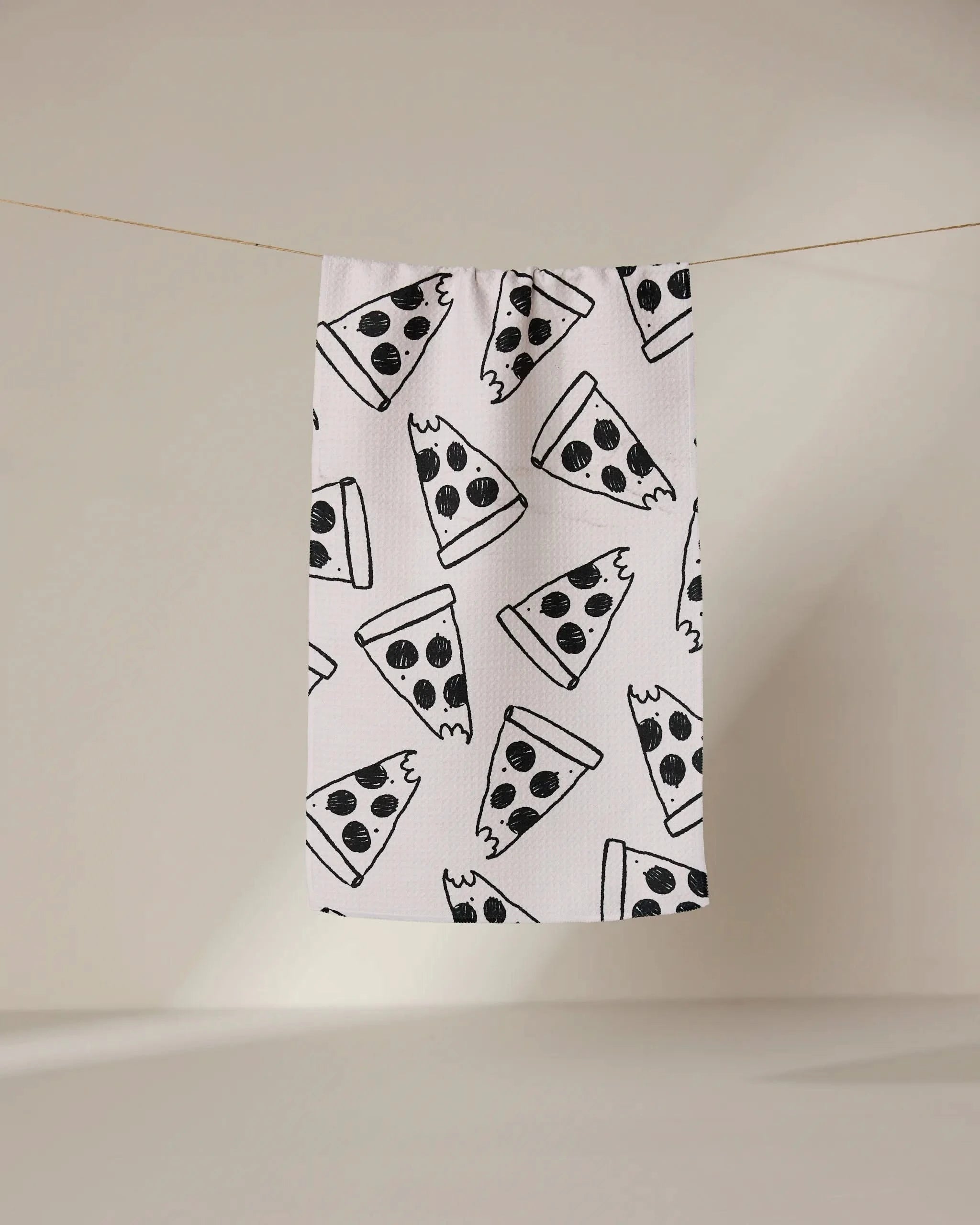 The Cole Strem Eternal Slice bar towel, made from soft Geoweave fabric, hangs on a line and showcases a repeating black cartoon pepperoni pizza slice pattern on white.