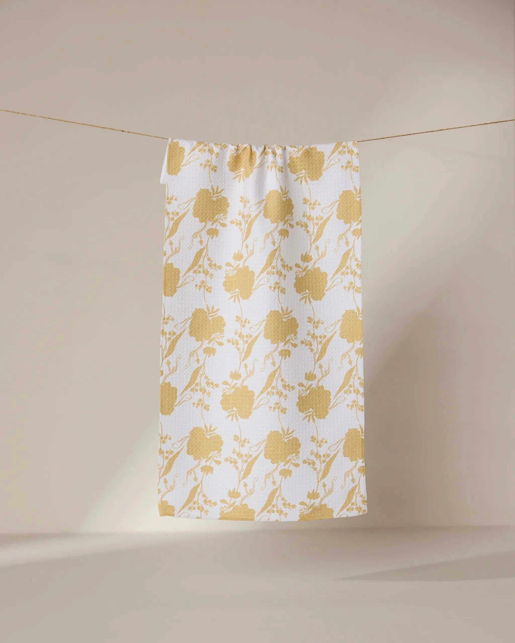 The GEOMETRY Eternal towel, featuring a white ultra-absorbent textured surface with a repeating yellow floral pattern, hangs neatly on a clothesline against a neutral background.