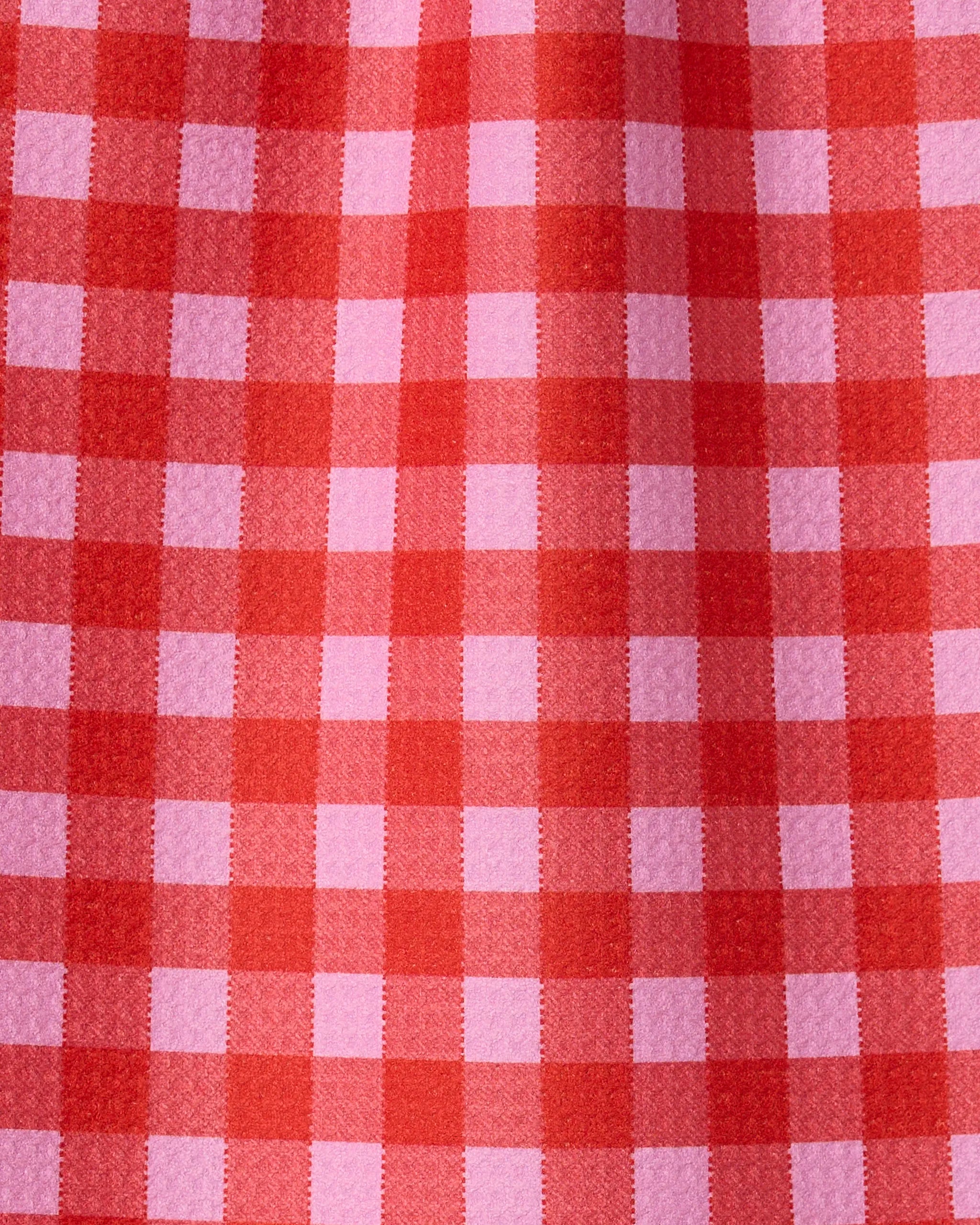 Close-up of Cherry Gingham by GEOMETRY, featuring a red and pink checkered pattern with visible texture, crafted from recycled materials and highlighted by fabric folds.