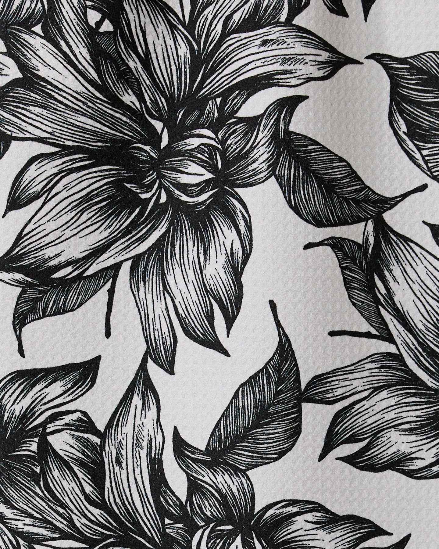 Black and white illustration of large, detailed flowers and leaves with intricate linework covers Caring by GEOMETRY, a textured recycled kitchen or bar towel.