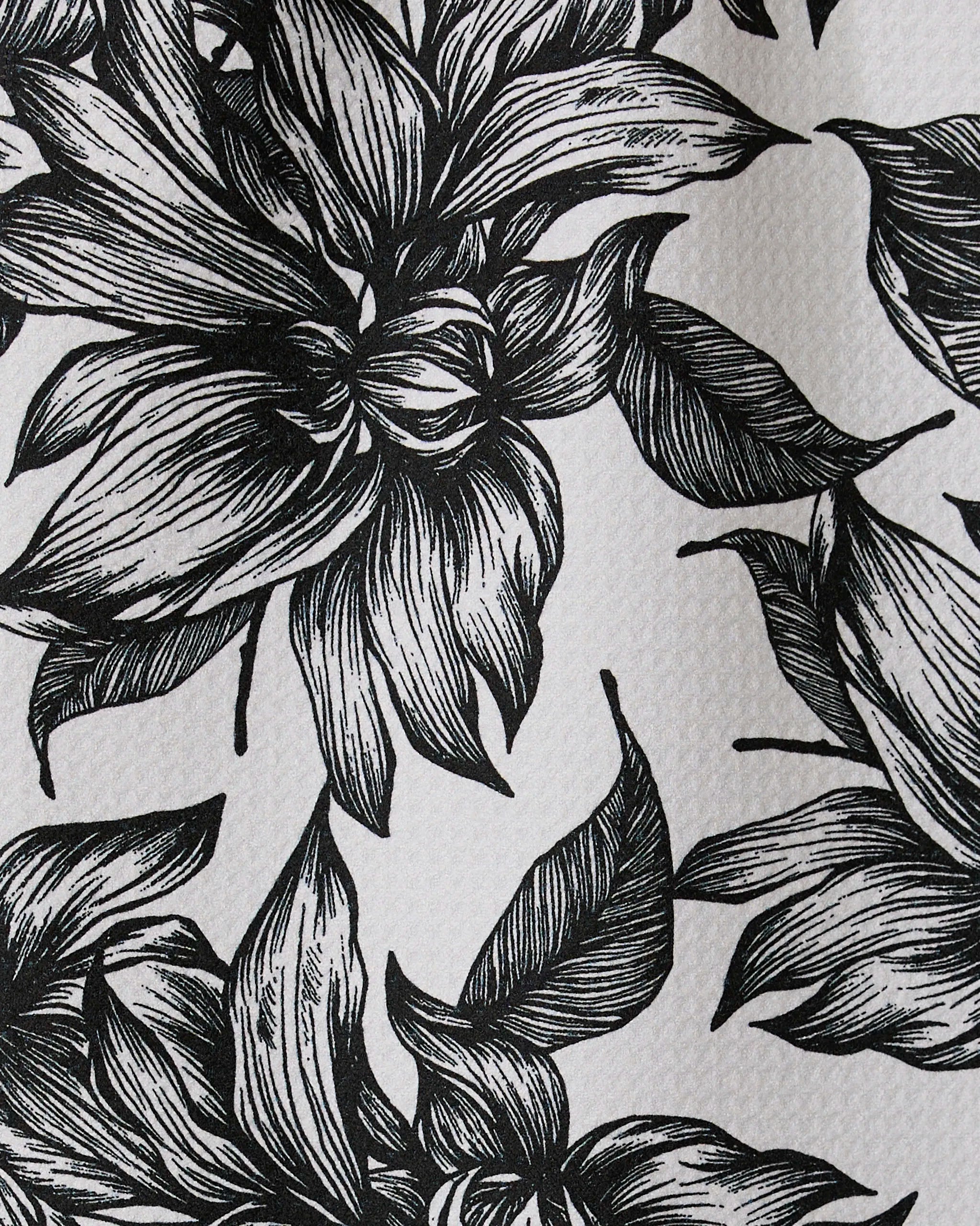 Black and white illustration of large, detailed flowers and leaves with intricate linework covers Caring by GEOMETRY, a textured recycled kitchen or bar towel.