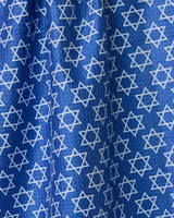 A blue double-sided tea towel from Geometry, called Star Of David, featuring an even pattern of white Stars of David. The fabrics folds and creases create varied light and shadow across the surface.