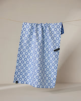 The Geometry Star Of David kitchen towel features a blue Star of David pattern on light blue, hangs on a clothesline with a visible black tag, and is made from recycled materials for quick drying.