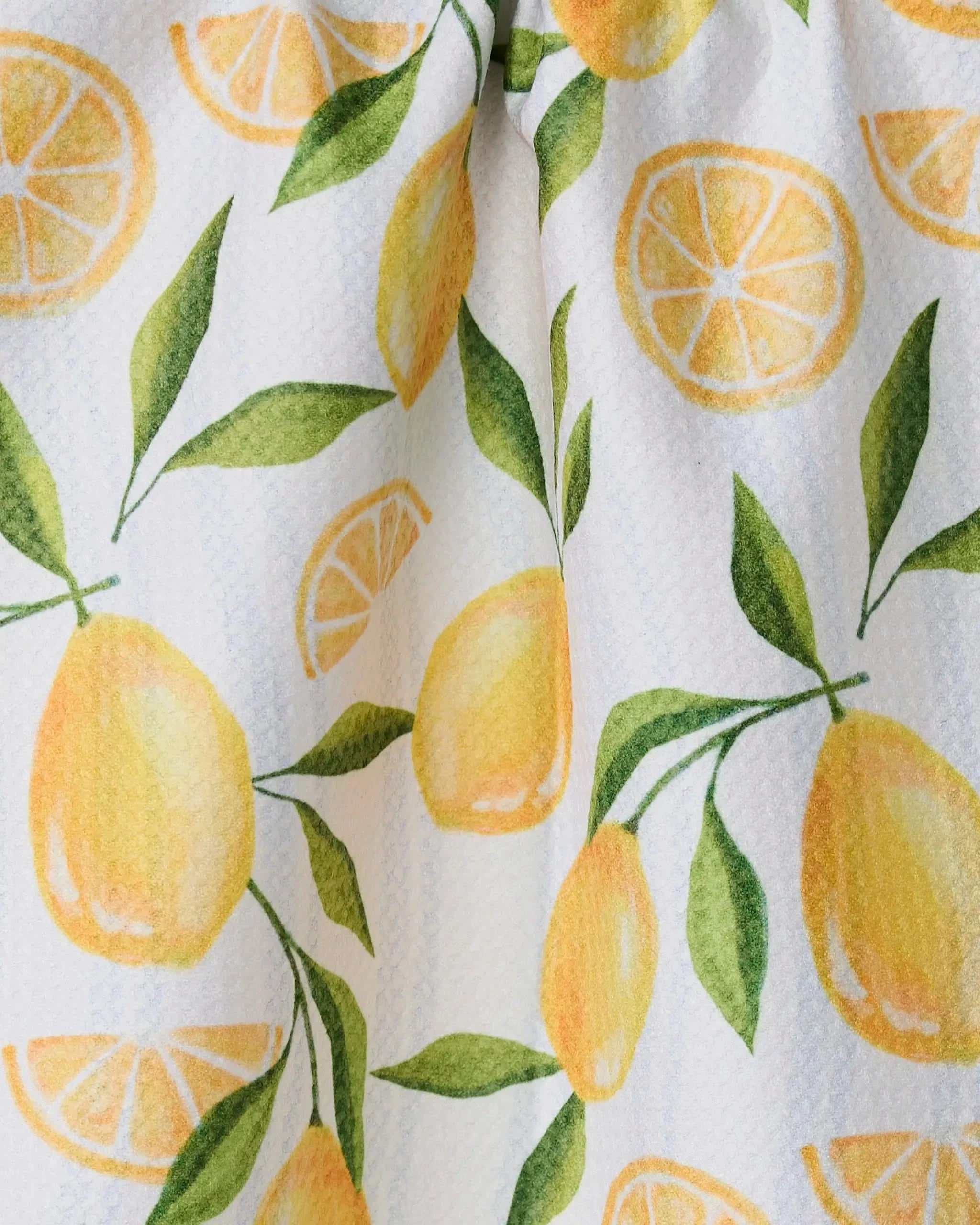 Geometry’s Lemon Bliss kitchen towel features a watercolor-style design with yellow lemons, lemon slices, and green leaves on white recycled fabric. Its slightly wrinkled texture adds charm to this absorbent, quick-drying towel.