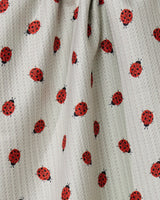A close-up of the Geometry Lady tea towel, made from quick-drying, light-colored textured fabric with a repeating red and black ladybug pattern. The material is gently gathered, creating soft folds and shadows.