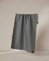 The Geometry Lady tea towel features black and white vertical stripes and a small red patch near the top right corner. It hangs double-sided on a thin clothesline against a neutral background.