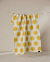 Geometry’s Energize recycled kitchen towel, featuring a repeating yellow sunburst pattern, hangs on a clothesline against a neutral background.