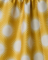 The Geometry Energize Absorbent Quick-Dry Towel features yellow fabric with a white sunburst pattern and is gathered at the top for gentle folds and shadows.