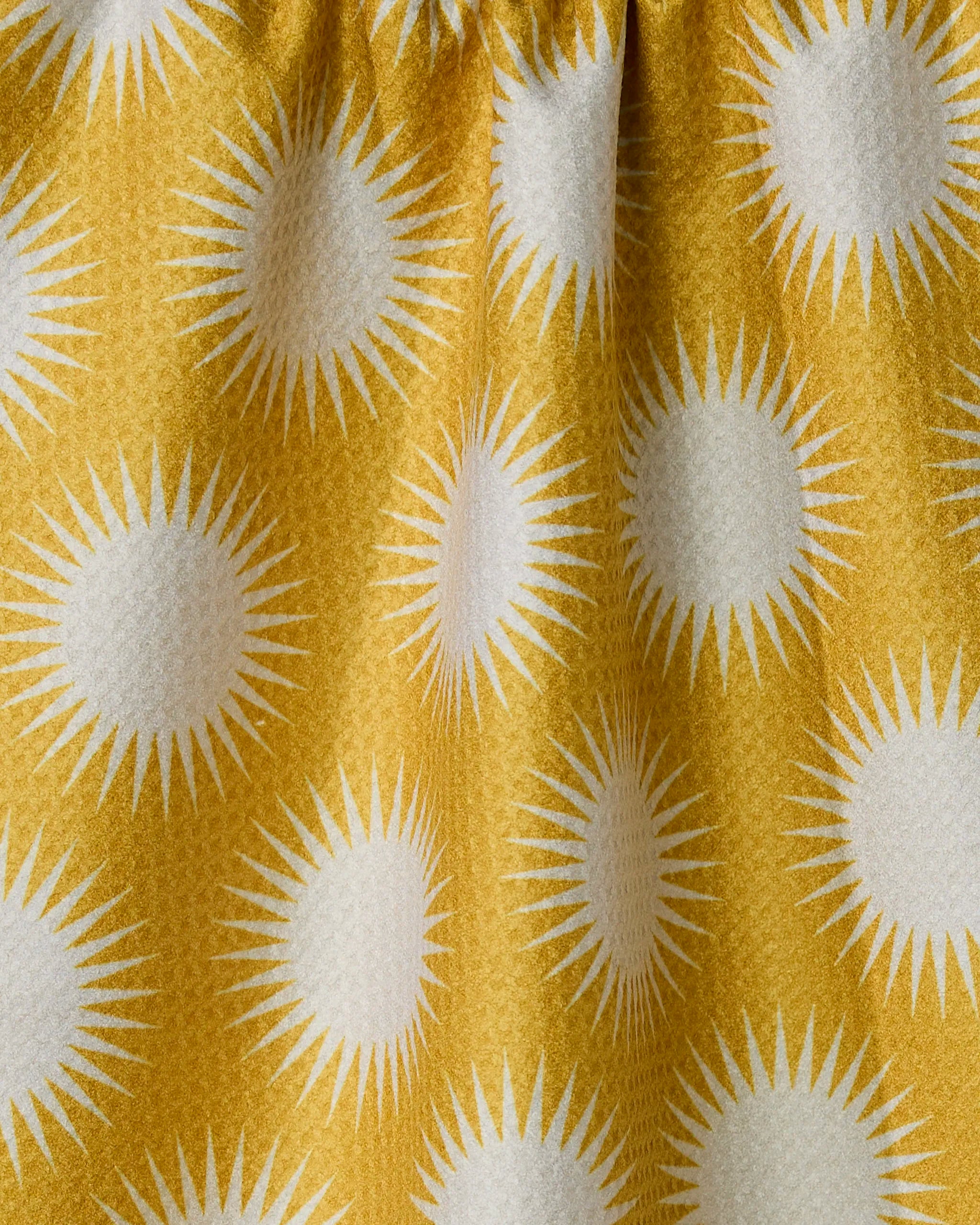 The Geometry Energize Absorbent Quick-Dry Towel features yellow fabric with a white sunburst pattern and is gathered at the top for gentle folds and shadows.