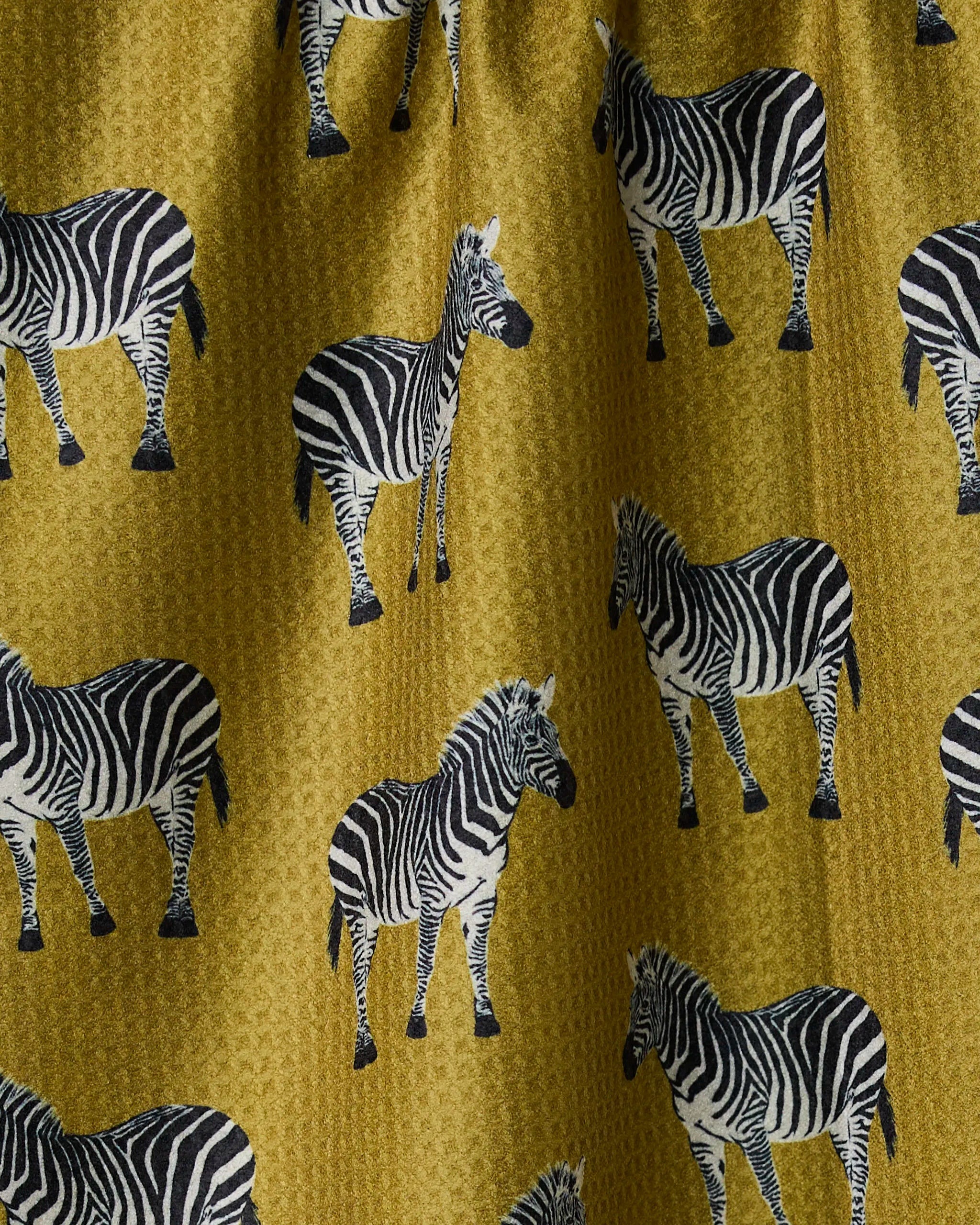 The Geometry Zebra Way tea towel is double-sided, featuring a mustard yellow background with a repeating pattern of black and white zebras in various poses and directions.