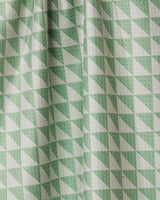 Close-up of Geometrys Pistachio Quick-Drying Tea Towel featuring a repeating pattern of green and white triangles. Subtle folds and shadows highlight the texture of this practical kitchen accessory.