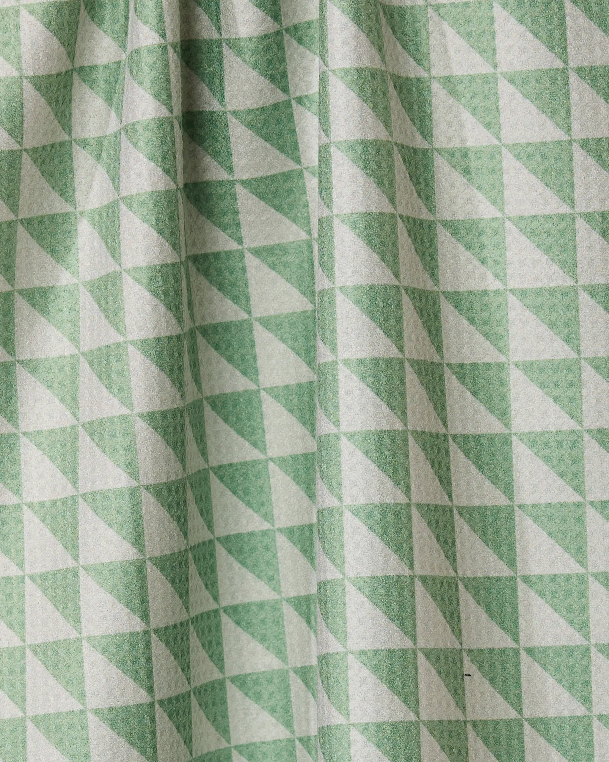 Close-up of Geometrys Pistachio Quick-Drying Tea Towel featuring a repeating pattern of green and white triangles. Subtle folds and shadows highlight the texture of this practical kitchen accessory.