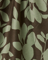 Geometry’s Eucalyptus tea towel features a dark brown background with a light green leaf and floral pattern, double-sided design, and a dimpled, waffle-like texture for extra absorbency.