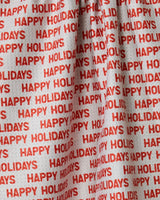 The Geometry Holiday 2024 towel is made of white fabric with repeated red HAPPY HOLIDAYS text in all caps, arranged in horizontal rows. Absorbent and quick-drying, its festive look is enhanced by the gathered or folded sections.