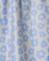 A close-up of Geometry’s Peri fabric reveals a textured surface with pale blue, stylized flowers on a light gray background—ideal for a double-sided or quick-drying tea towel.