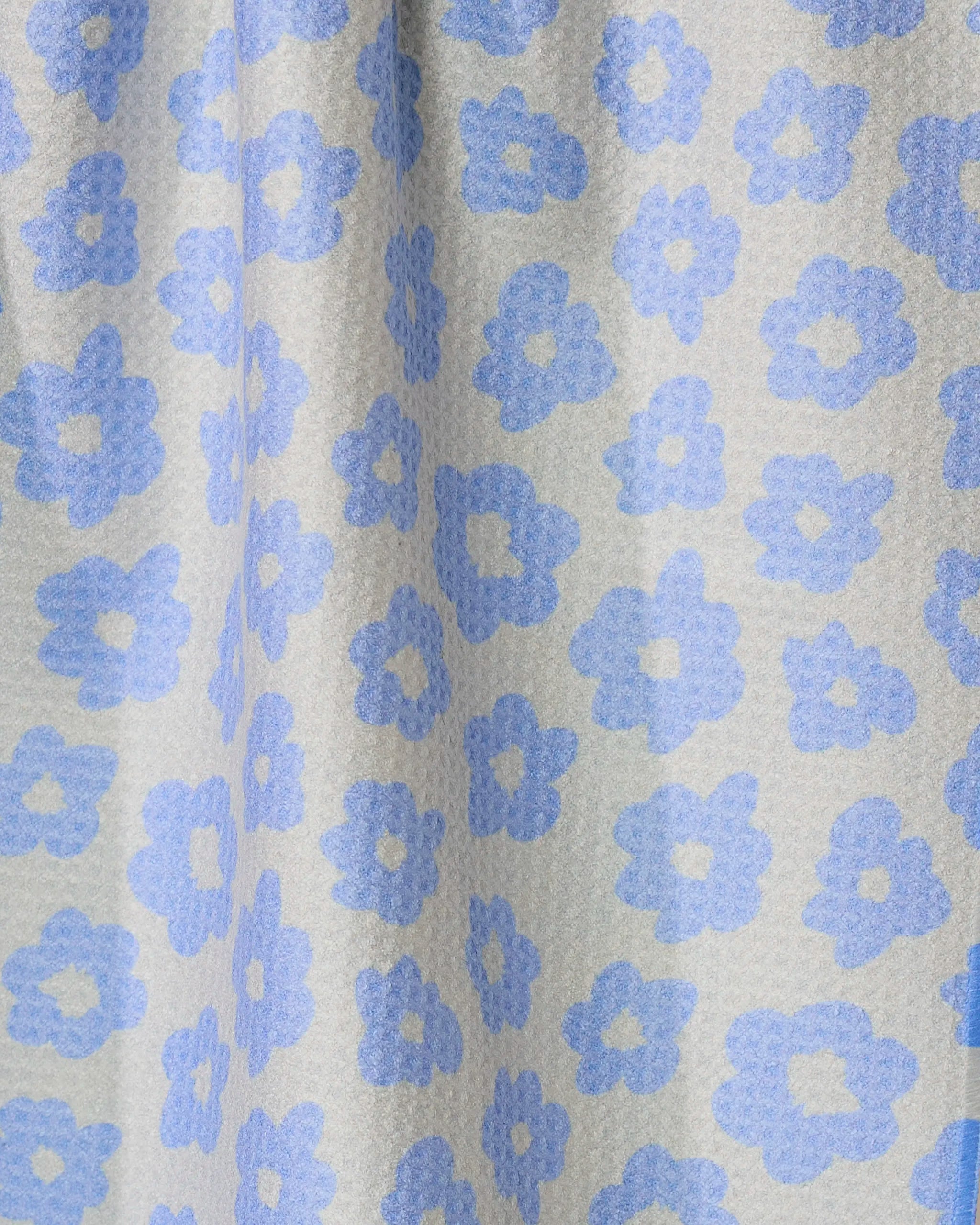 A close-up of Geometry’s Peri fabric reveals a textured surface with pale blue, stylized flowers on a light gray background—ideal for a double-sided or quick-drying tea towel.