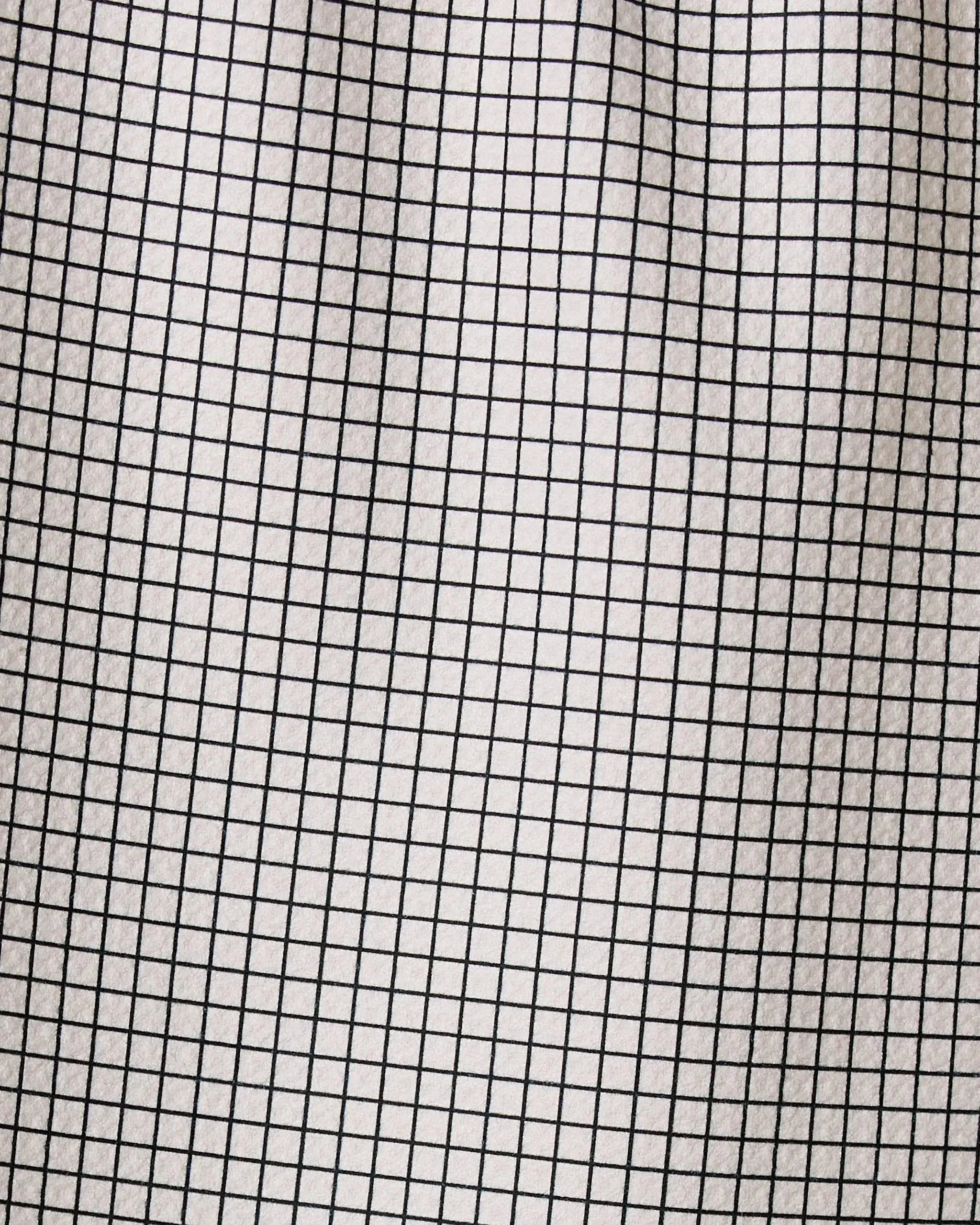 A close-up of Geometry’s Ian recycled kitchen towel fabric shows a black grid of thin, evenly spaced lines on white, forming small squares with visible folds and subtle shadows.