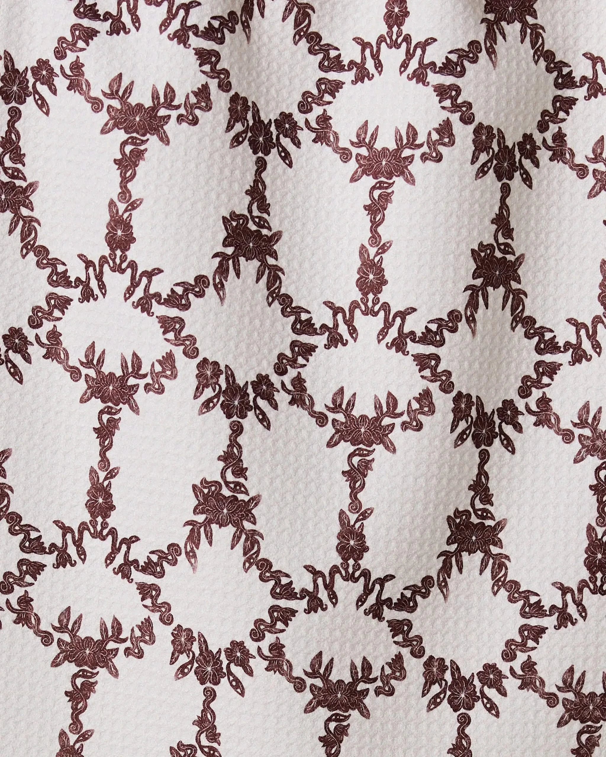 The Geometry Eye on You Floral bar towel features a burgundy symmetrical floral pattern with curved lines and ornate circular details, repeated on a white textured surface and crafted from recycled materials.