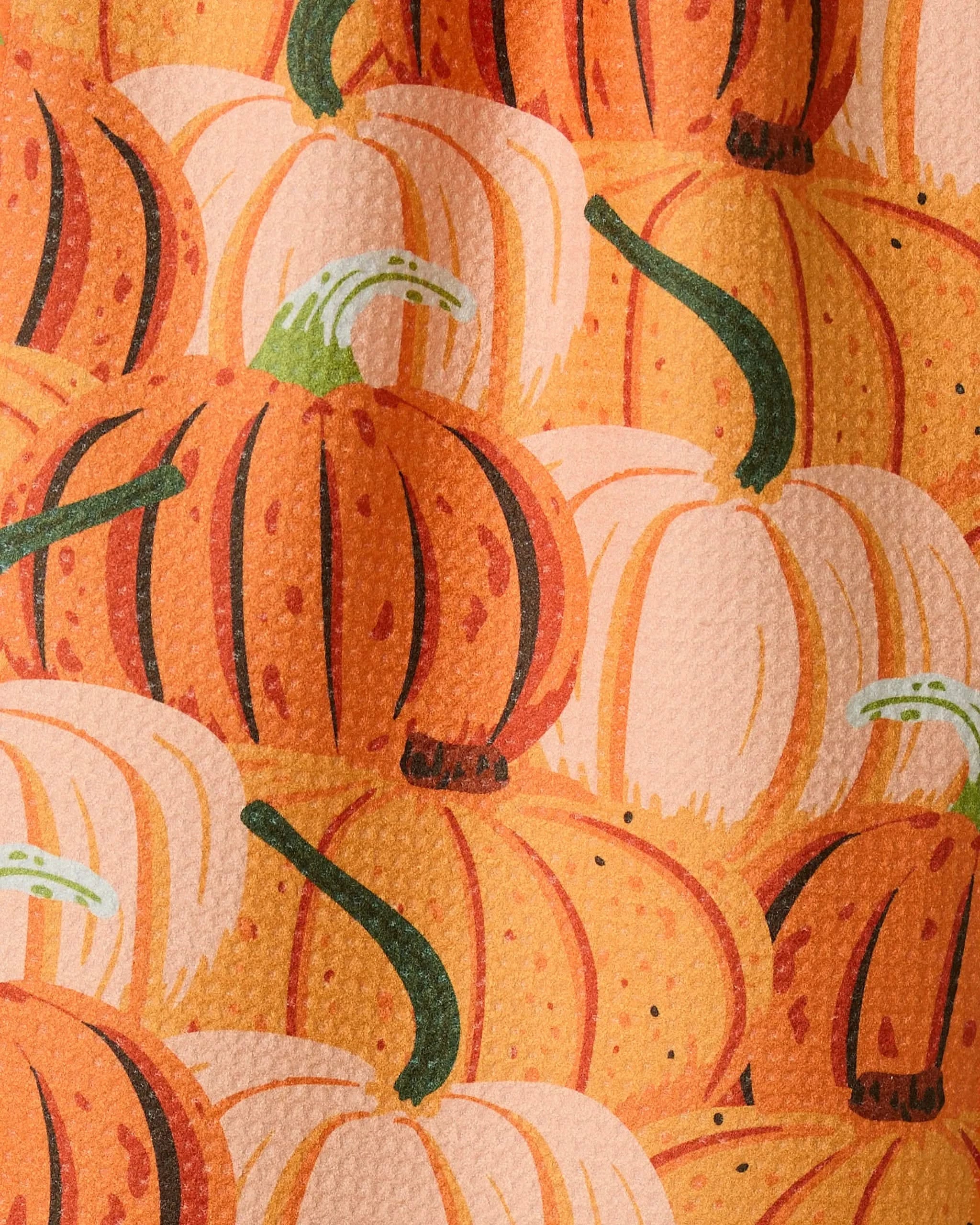 A close-up of Geometry’s Rows of Gourds recycled kitchen towel, featuring a textured surface with illustrated orange and white pumpkins with green stems overlapping in the pattern.