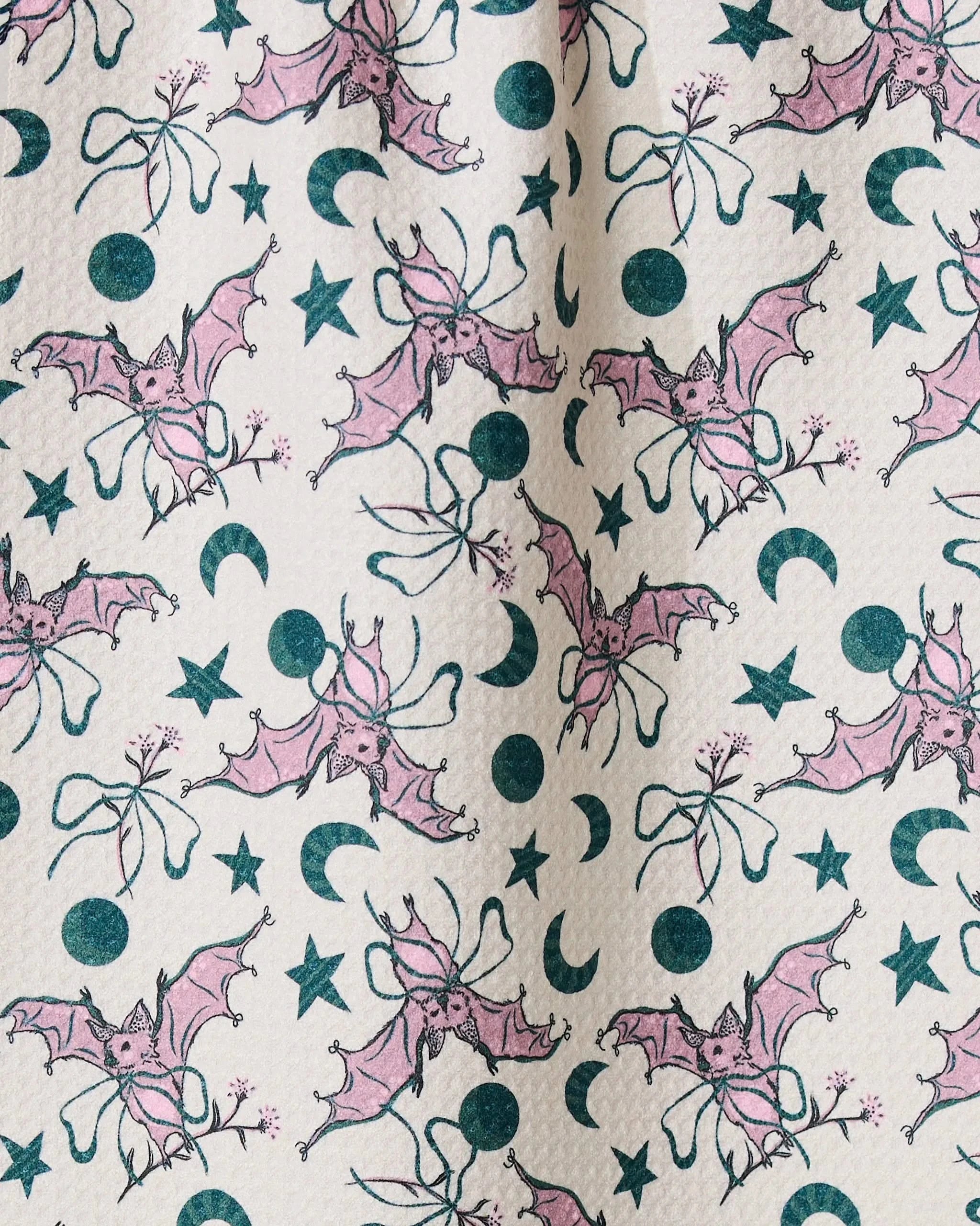The Geometry Bats with Bows recycled kitchen towel features a fun, evenly repeating pattern of pink bats, green stars, crescent moons, and bow shapes on a light background—an eco-friendly addition to your kitchen.