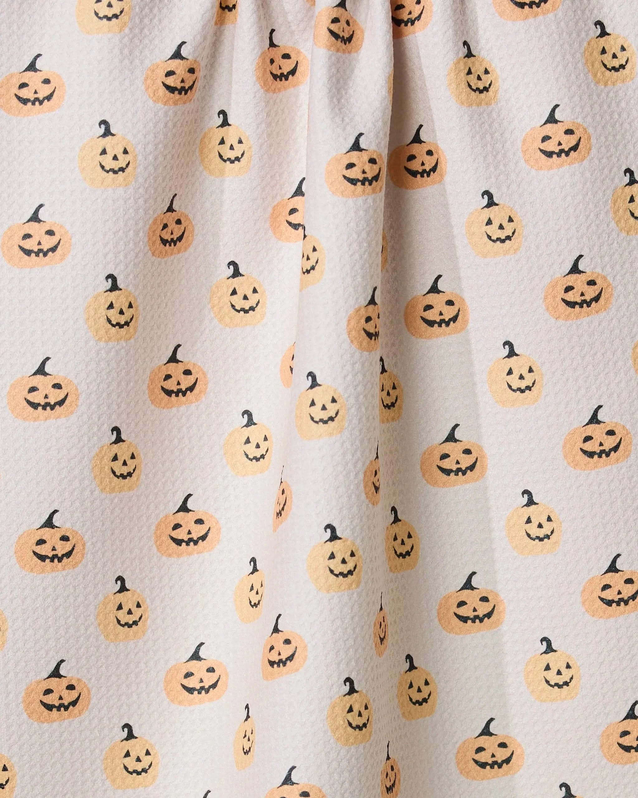 Geometry’s Spices and Smiles tea towel features white textured fabric with a cheerful orange jack-o’-lantern pattern, adding a festive Halloween touch to your kitchen with ultra-absorbent style.