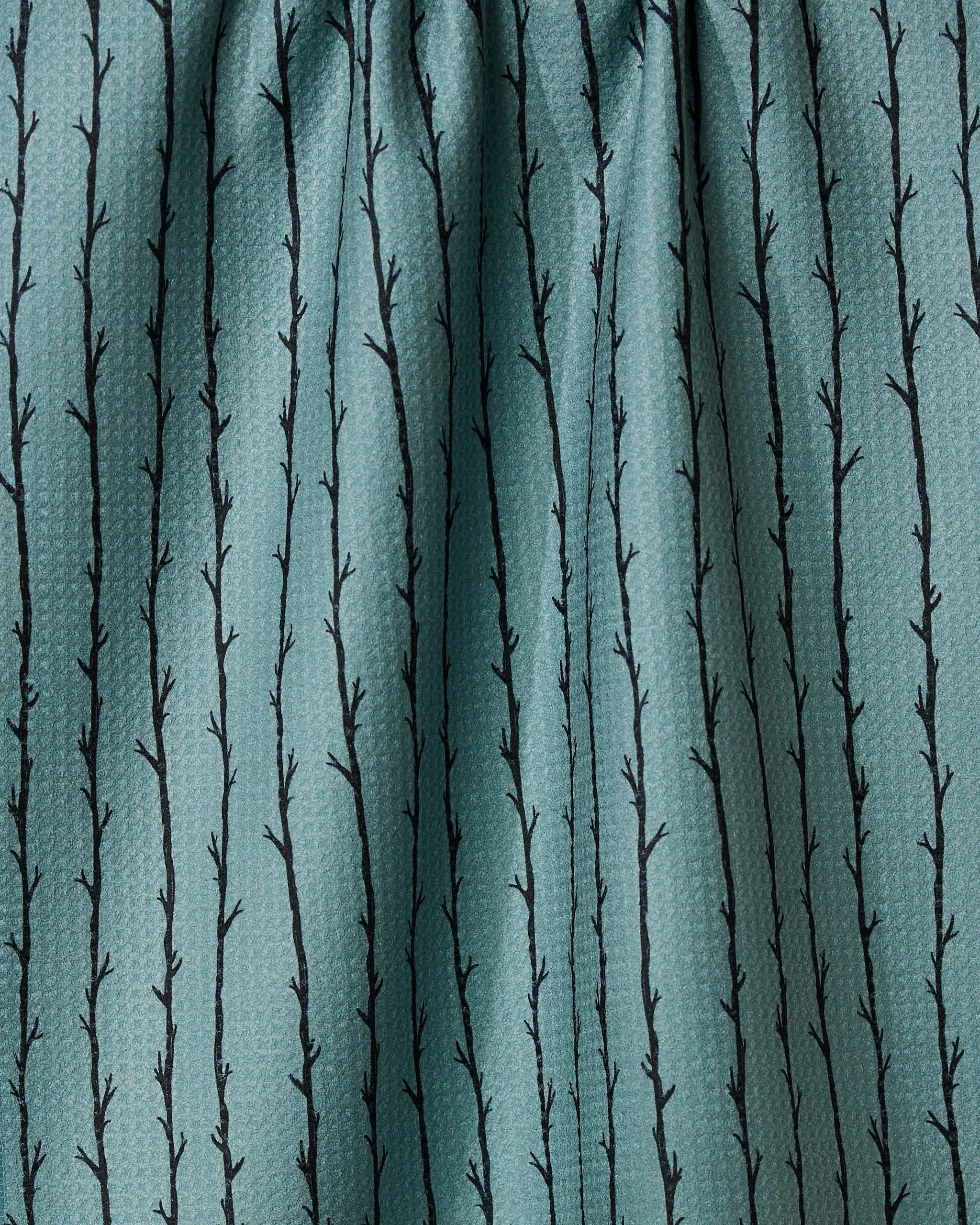 A close-up of Geometry’s Branch Stripes fabric shows teal, slightly textured, quick-drying material with a gathered look and black vertical branch patterns featuring small offshoots.