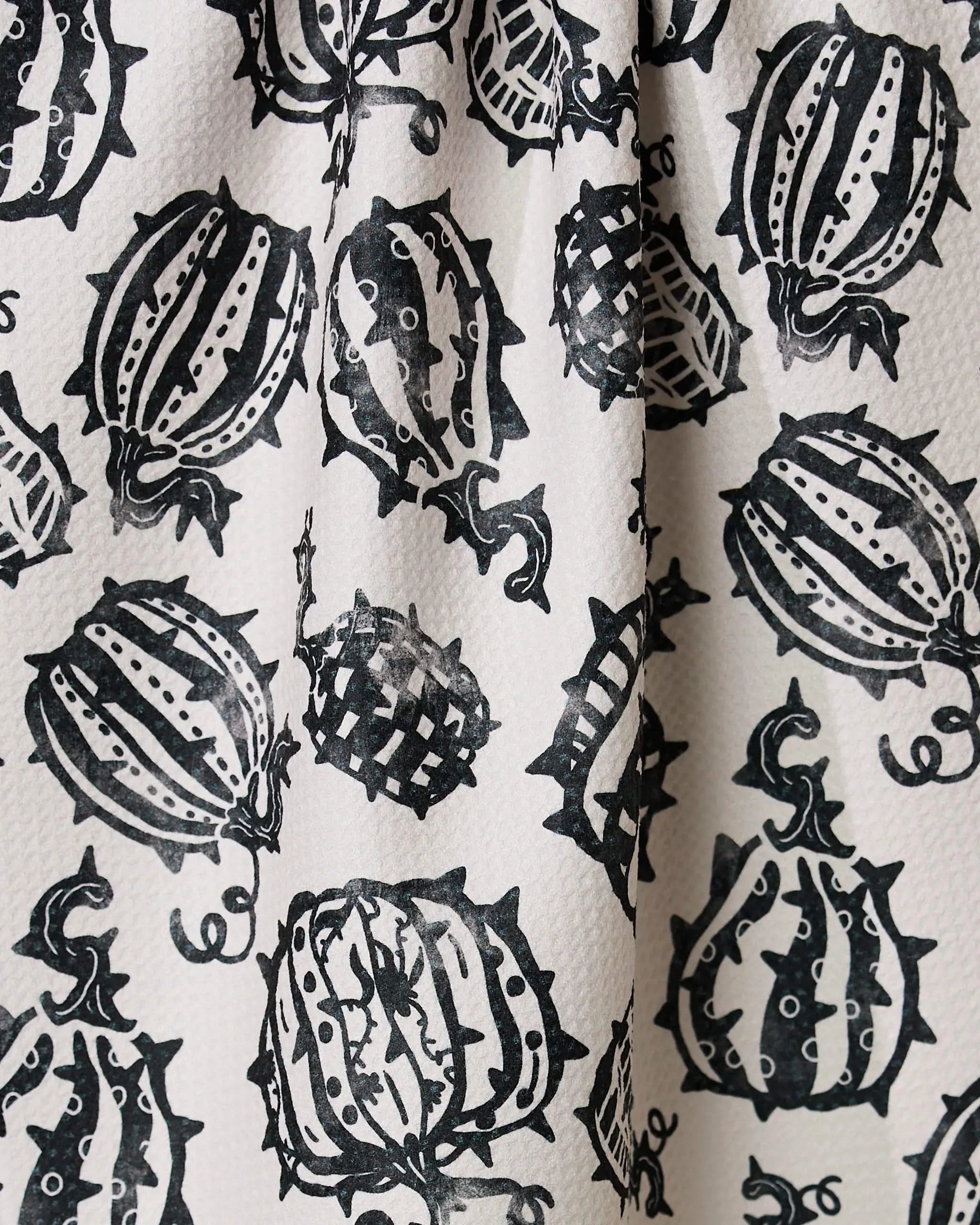 Geometry’s Punk Pumpkins kitchen towel features black ink illustrations of pumpkins and stylized vines, printed in a repeating pattern on white textured fabric with visible folds.