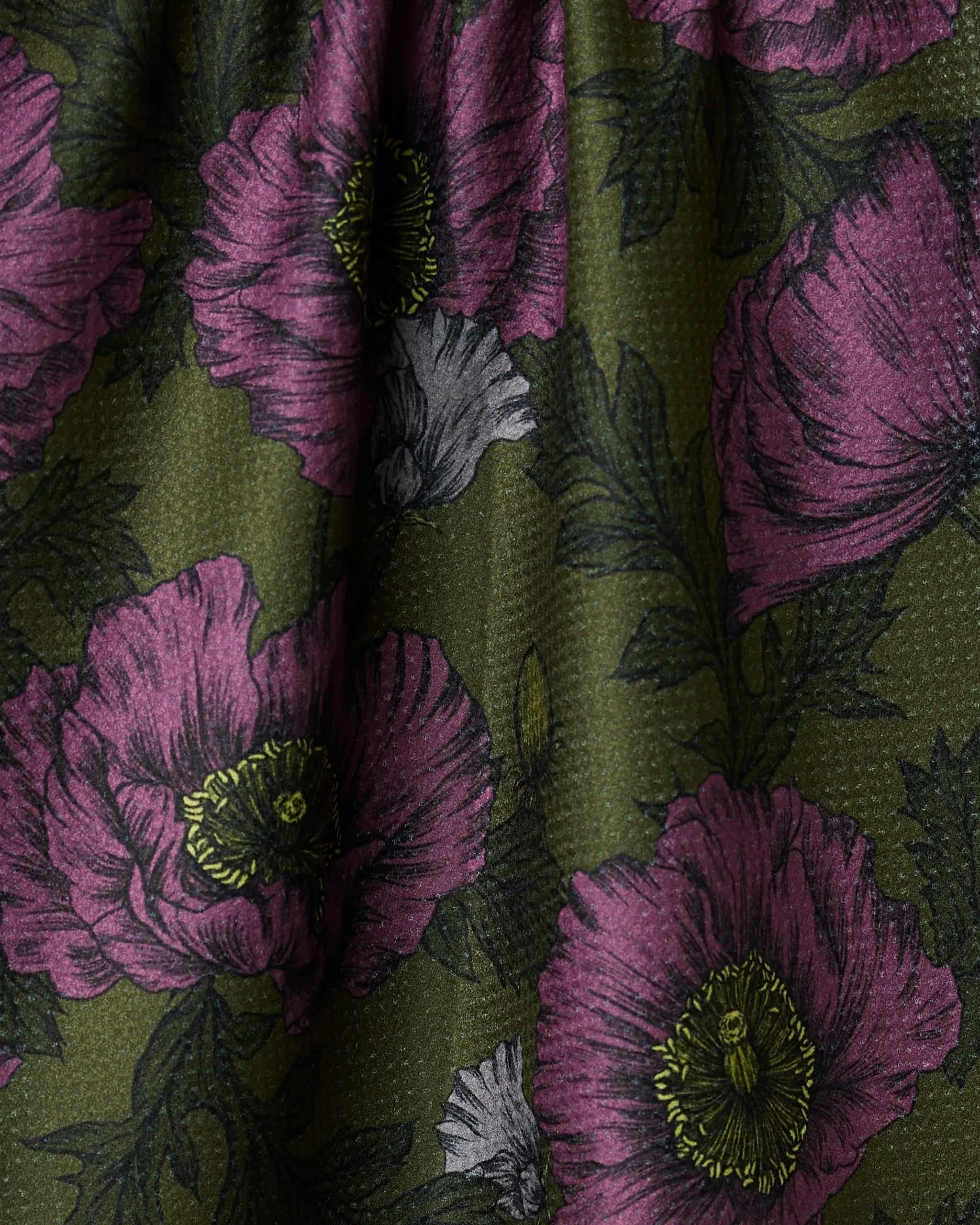 Close-up of Potion Poppies by Geometry: green recycled fabric with a textured surface, large purple flowers with yellow centers, dark green leaves, and a few small white flowers.