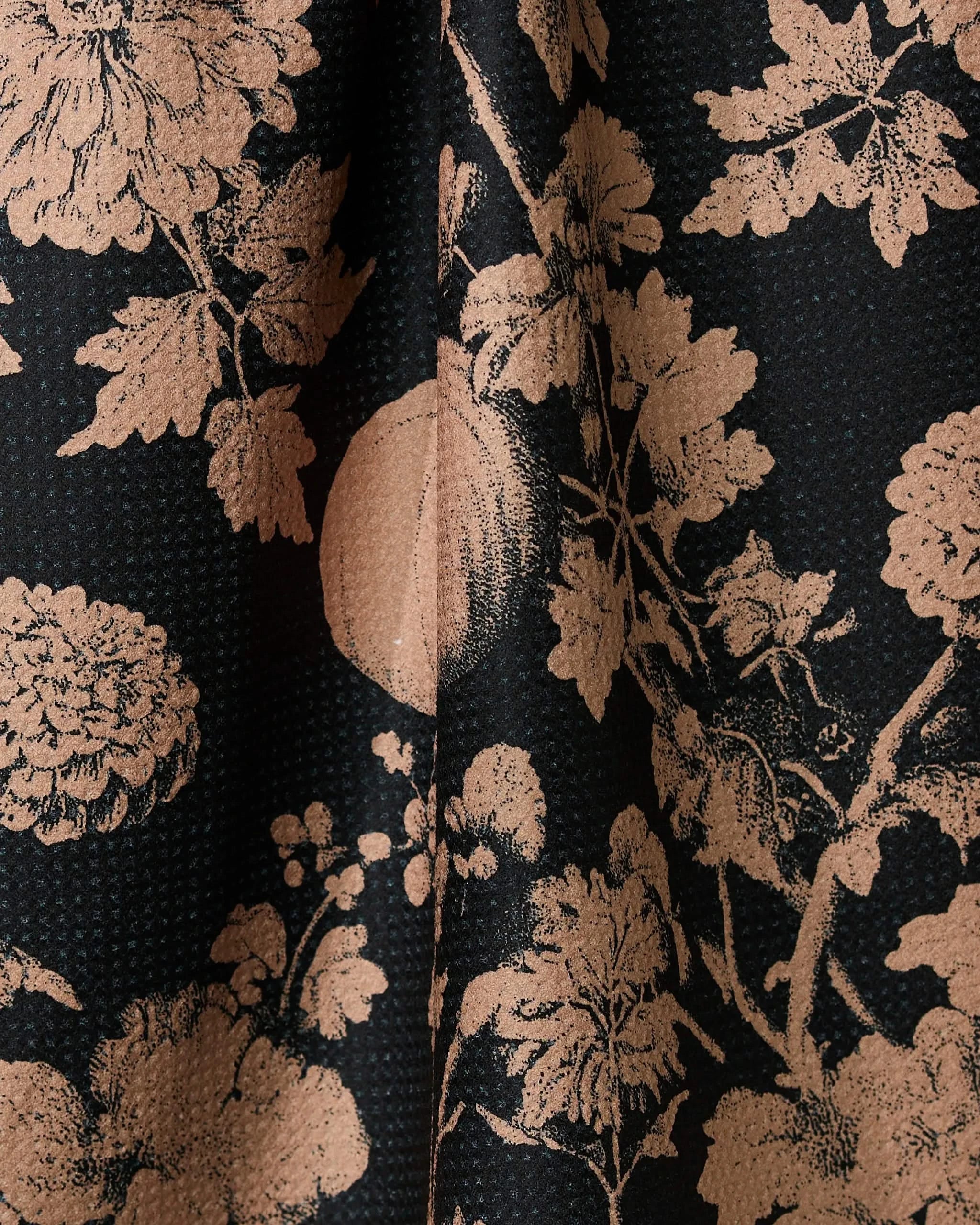 Close-up of Geometrys Haunted Harvest tea towel in black with a light brown floral and botanical pattern. Made from quick-drying, recycled materials, the fabric drapes softly in vertical folds.