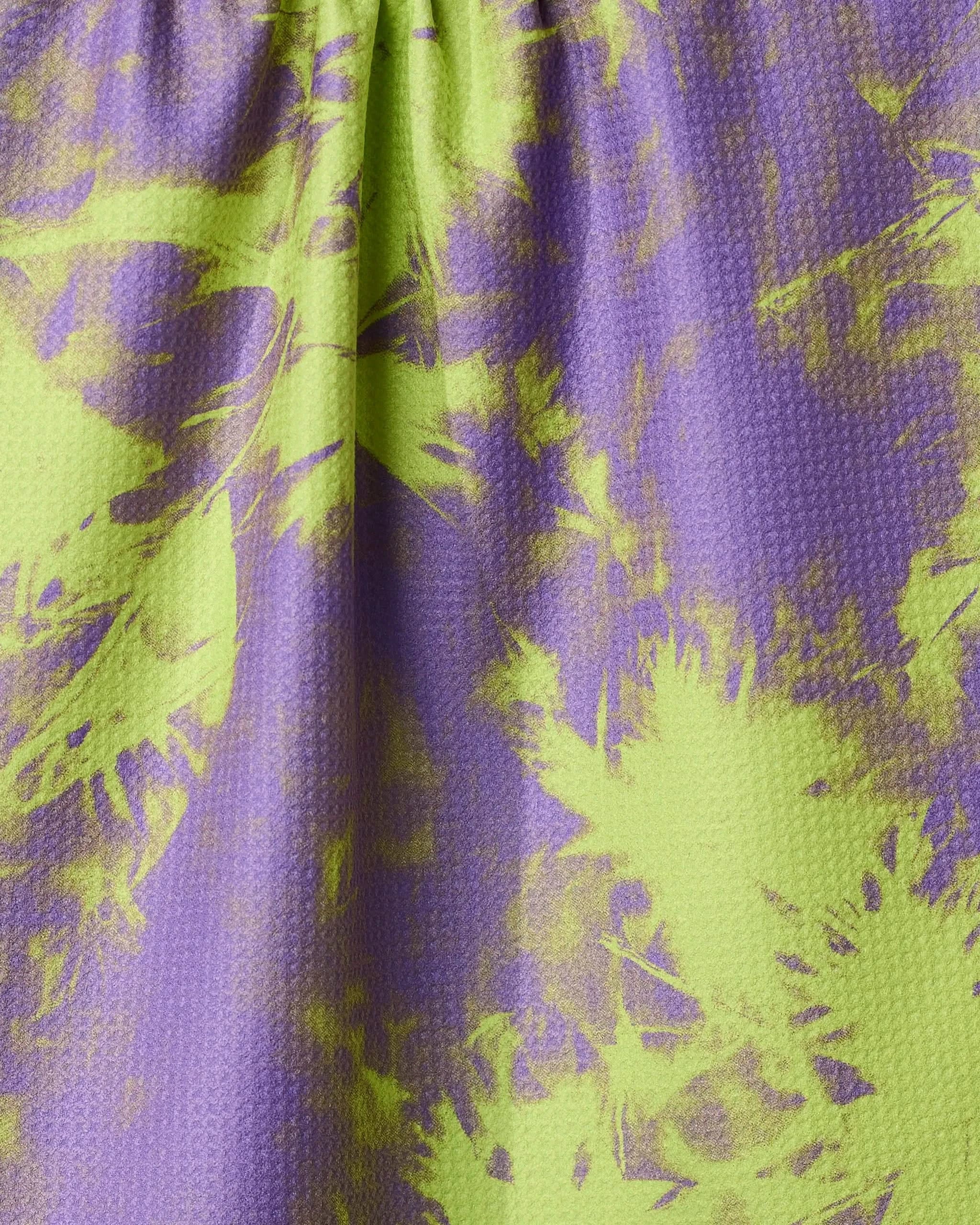A close-up of Potion Purple by Geometry, a tea towel with textured fabric and a yellow-green and purple tie-dye pattern featuring abstract shapes and soft blends.