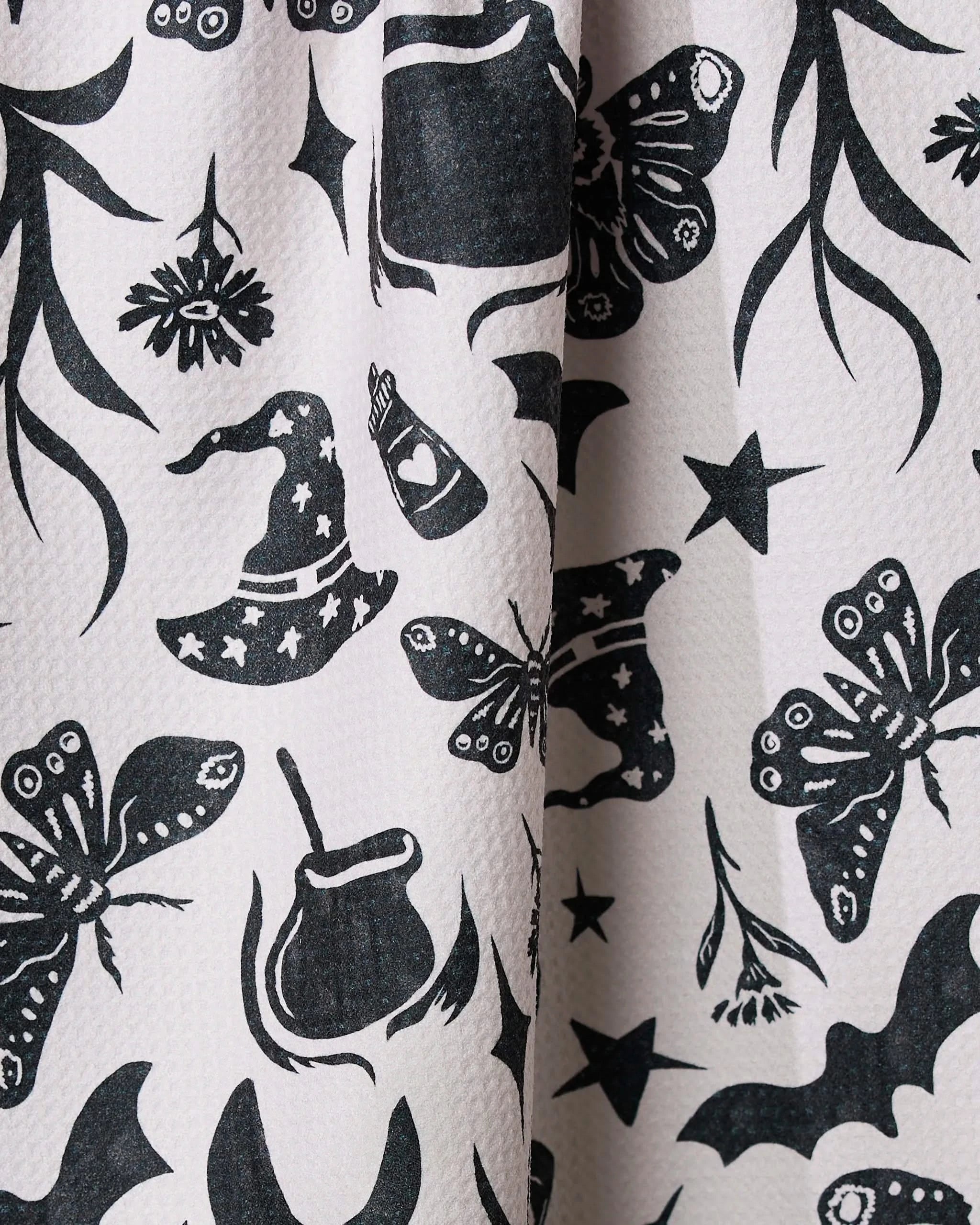 Moths, witch hats, bats, stars, potion bottles, flowers, and leaves decorate the whimsical Moths and Things tea towel by * UPDATE TO ARTIST NAME OR GEOMETRY. Made from recycled materials with a light textured fabric and magical repeating patterns.