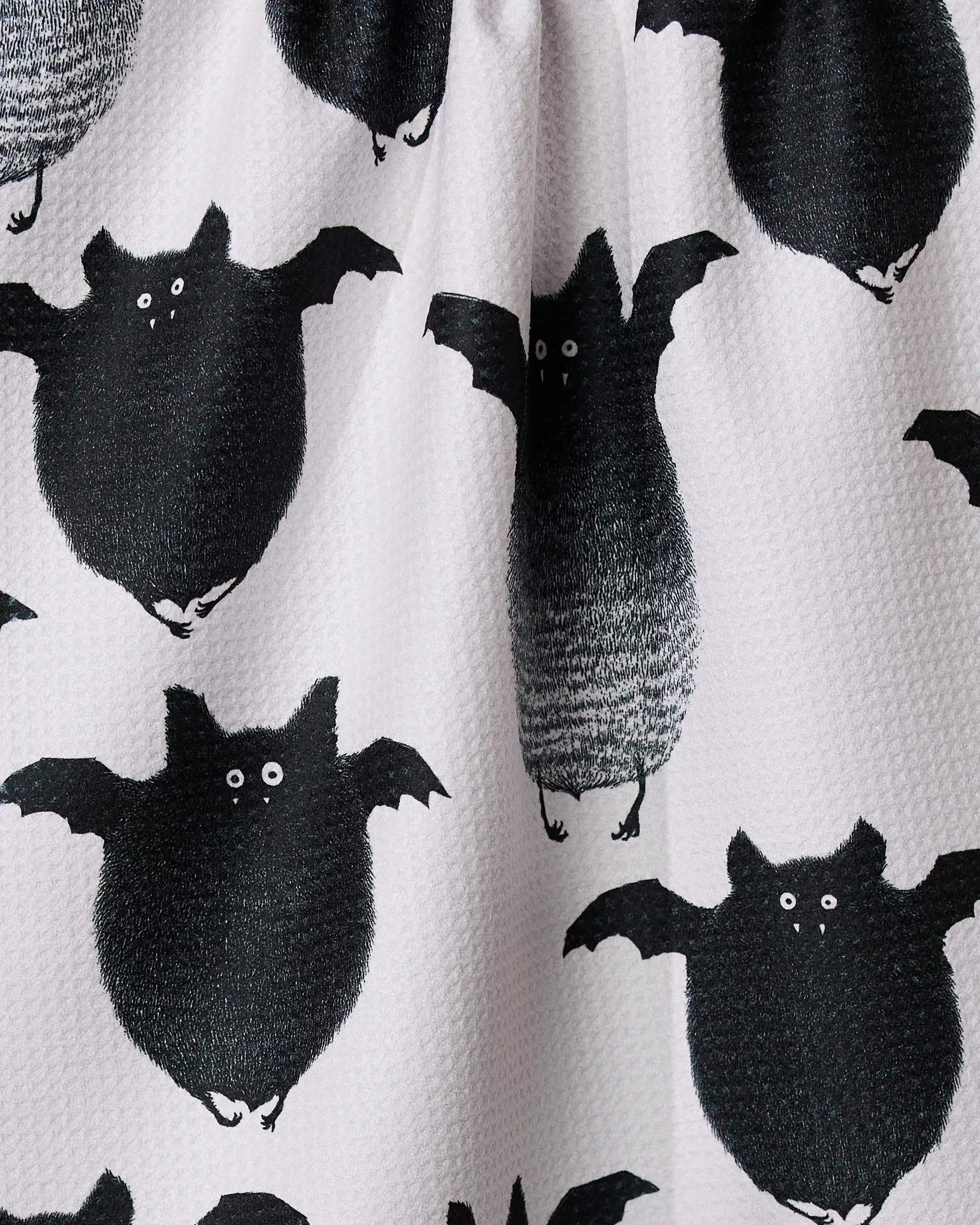The Geometry Fuzzy Bats towel features a white textured surface with playful black bats, each sporting round bodies, wide wings, and big white eyes for a whimsical touch.