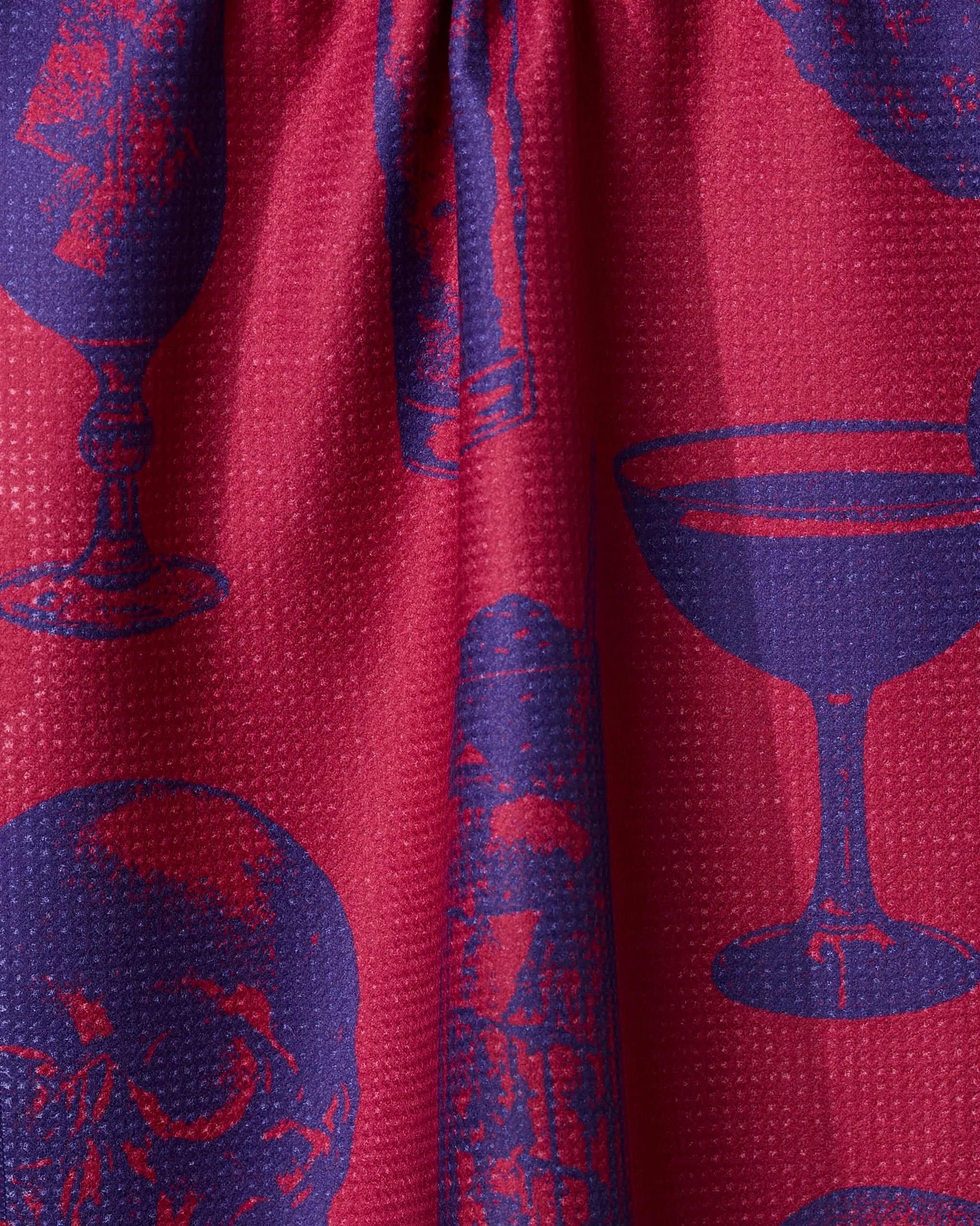 The Ghostly Cheers Red tea towel by Geometry features bold purple skulls, wine glasses, and candles on red textured fabric with gathered folds—an eye-catching piece that adds graphic style and flair to your kitchen.