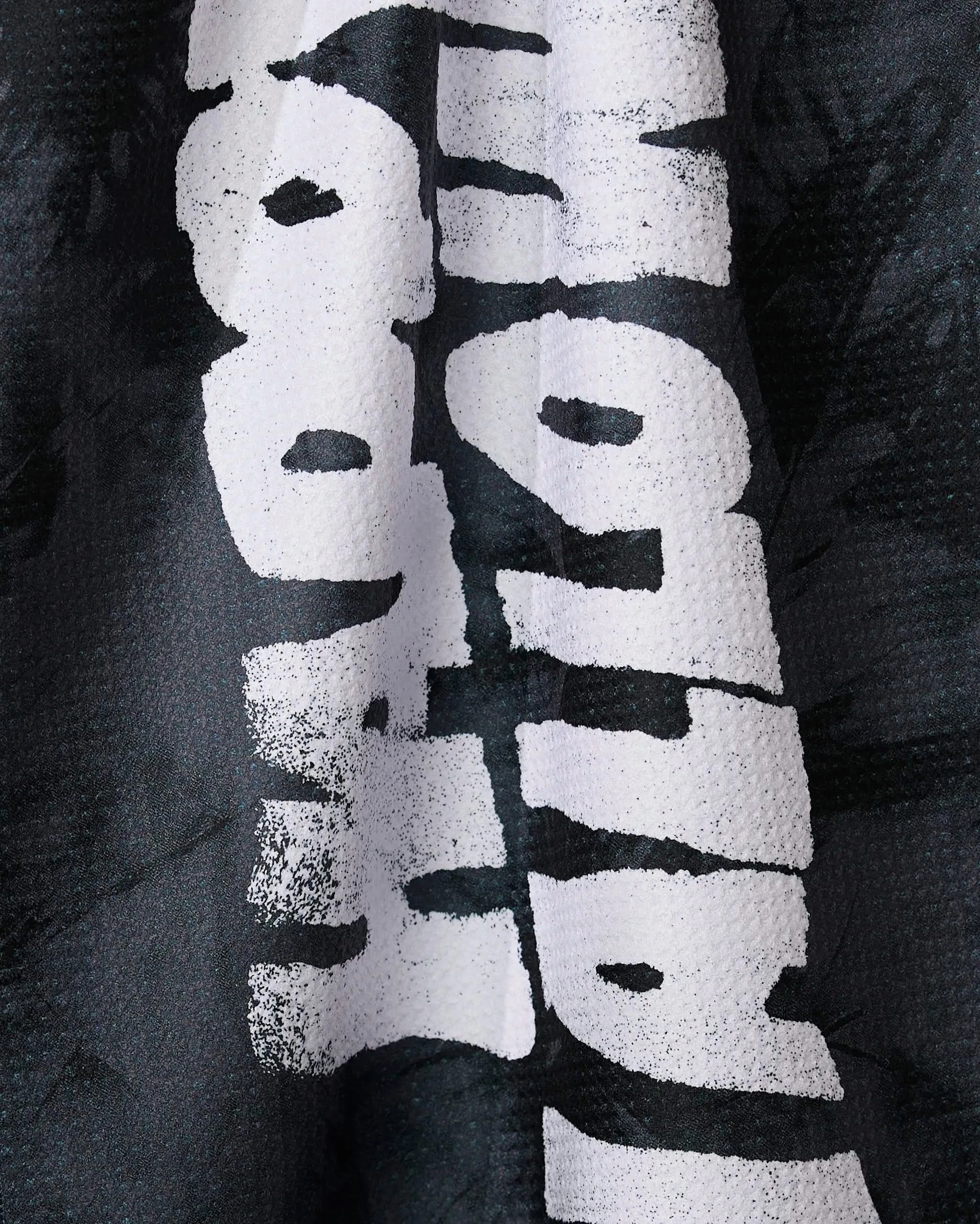 Close-up of the Geometry Happy Halloween Night tea towel in black, featuring bold, white, distressed vertical text. Folds and texture obscure some letters on this absorbent towel made from recycled materials.