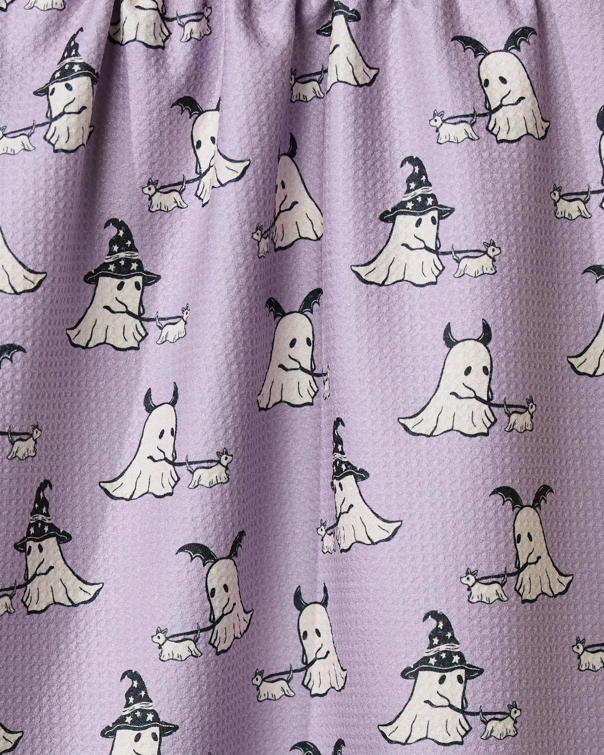 Spooky Ghost Walk by Geometry is a light purple tea towel made from recycled materials, featuring cartoon ghosts in witch hats walking small white dogs. The textured, quick-drying fabric has black outlines for a playful look.
