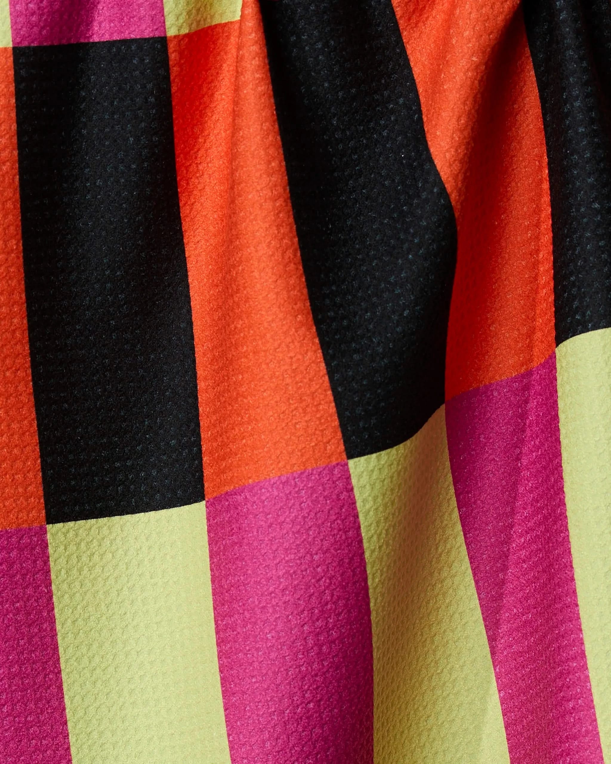 Close-up of Geometrys Spooky Hour Stripe tea towel, featuring a bold checkerboard pattern in black, orange, pink, and yellow on ultra-absorbent textured fabric with a slightly wrinkled look.