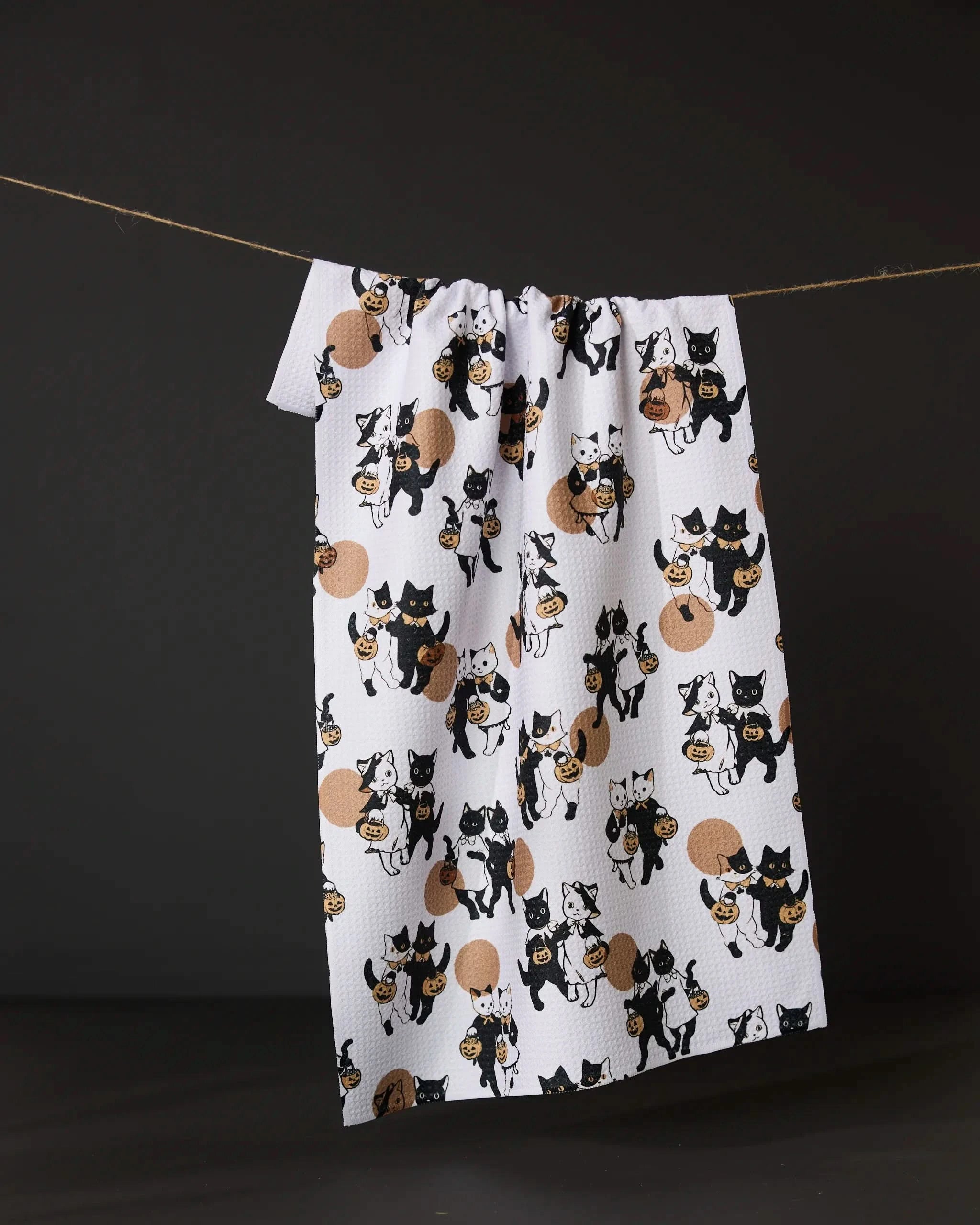The Geometry Halloween Date tea towel dries quickly and displays playful cartoon black and white cats—some with brown yarn balls—hanging on a clothesline against a dark background.