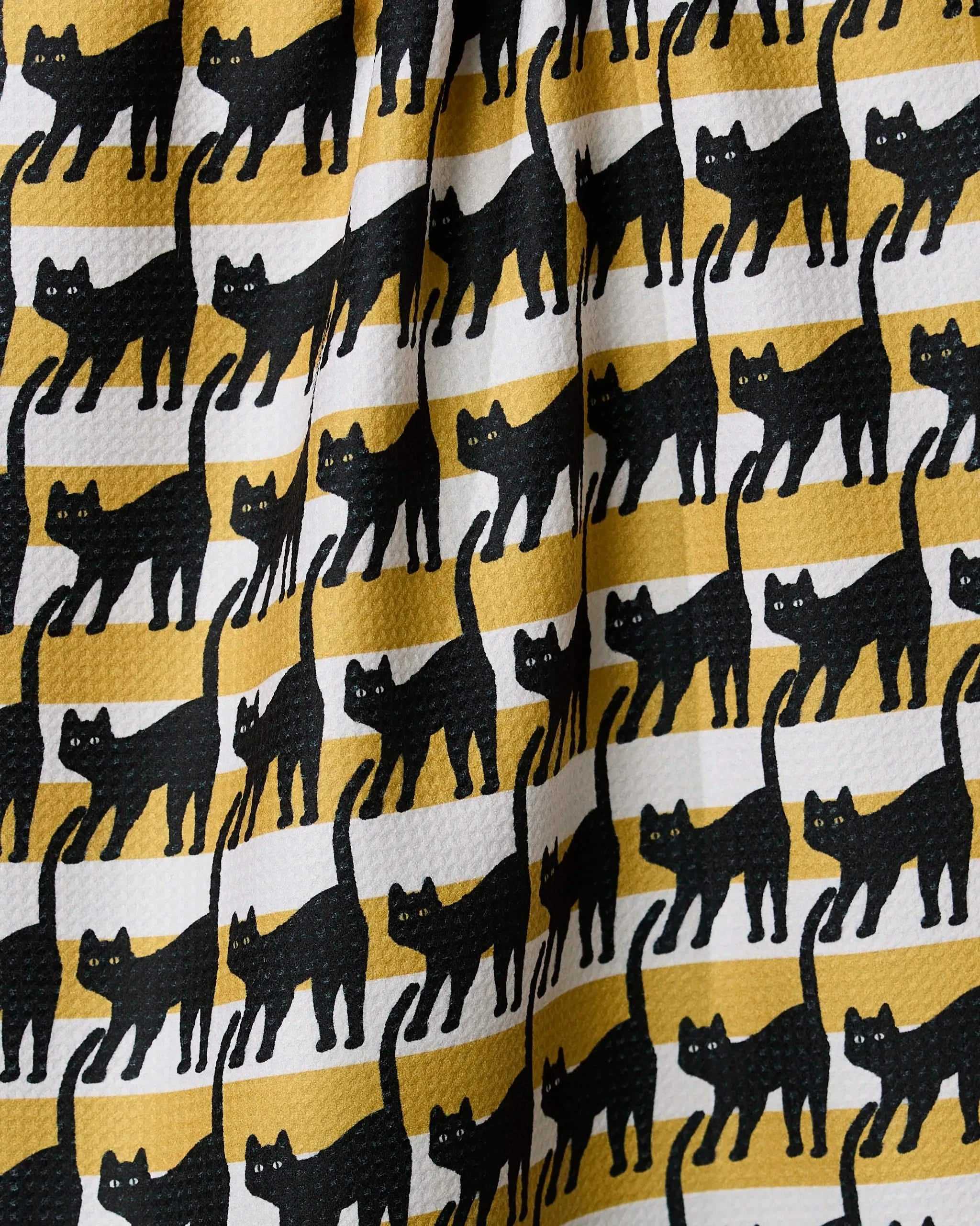 The Geometry Salem Cat Stripe tea towel features rows of black cats with raised tails on alternating yellow and white stripes. Its textured, slightly wrinkled surface makes it an eco-friendly choice for any kitchen.