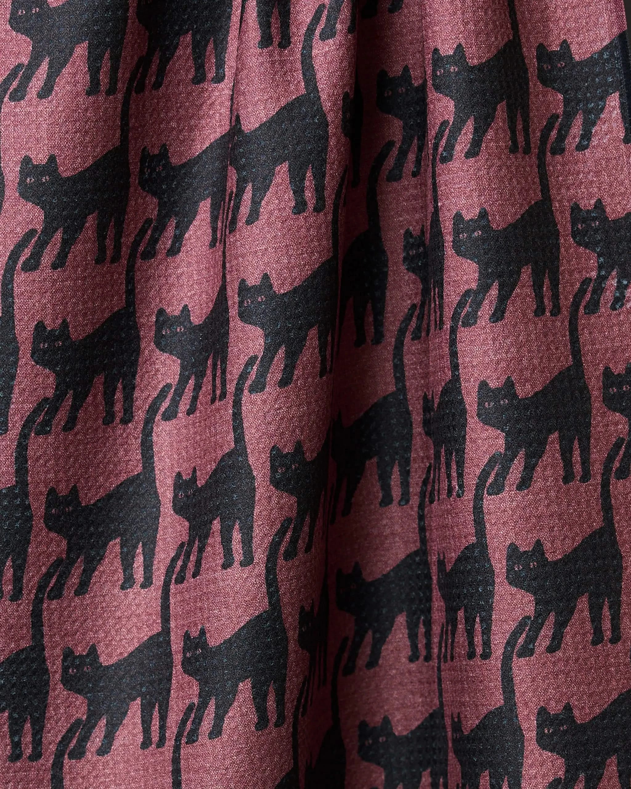 A close-up of the Geometry Salem Cat kitchen tea towel, made from recycled materials. It features a repeating pattern of black cats with arched backs on a reddish-brown background and slightly wrinkled fabric.