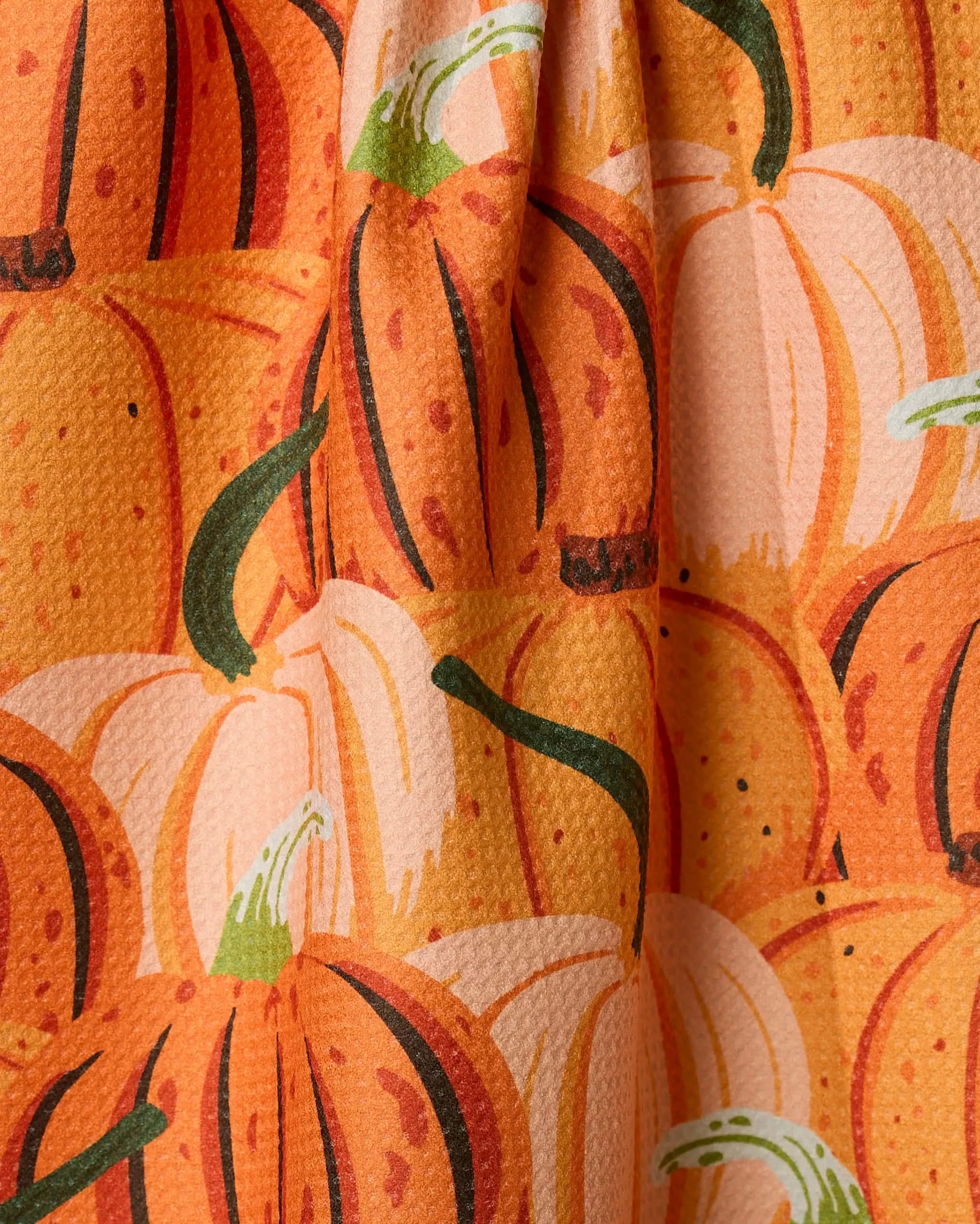 Close-up of Geometry’s Rows of Gourds ultra-absorbent tea towel in orange, showcasing a printed pattern of large overlapping pumpkins with green stems and a slightly textured finish.