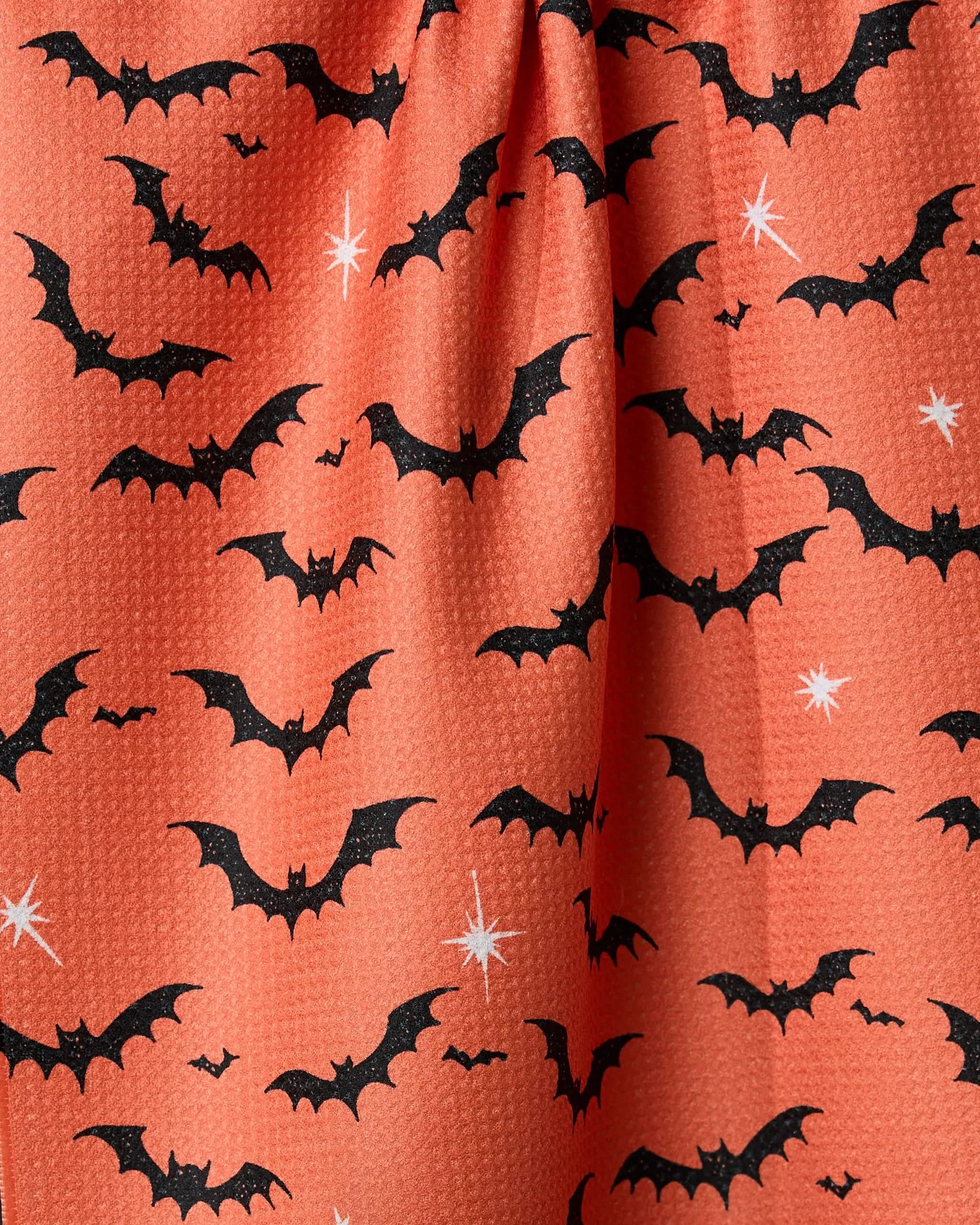 Geometry’s Midnight Friends Orange tea towel features black bats and white starbursts on orange fabric for a spooky, Halloween vibe. Made from recycled materials with a slightly textured top-gathered surface.
