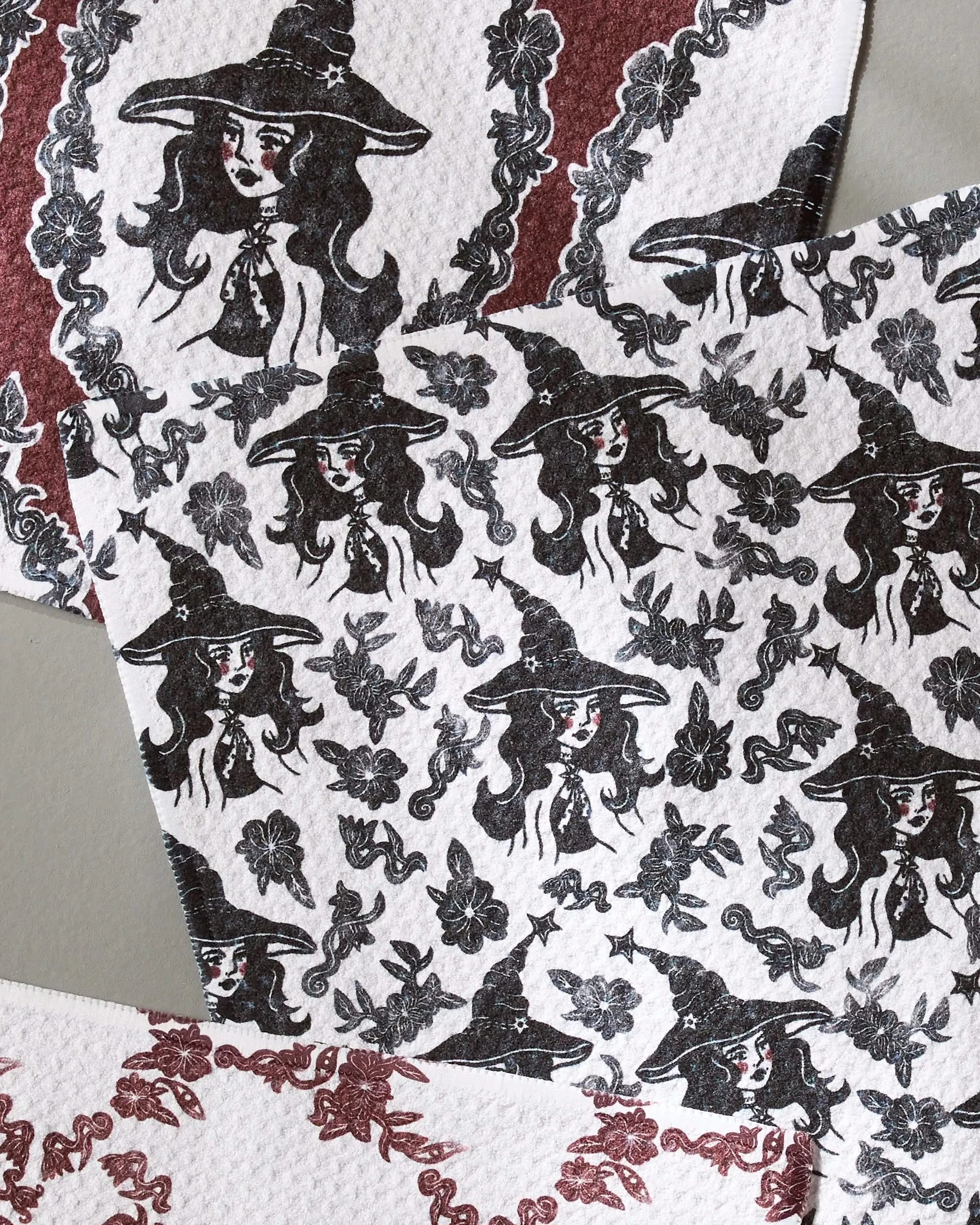 Geometry’s Witchy Blooms dishcloth set features super-absorbent towels with black illustrations of a woman in a witch hat amid leaves, flowers, and decorative borders—charming motifs repeated across every towel.