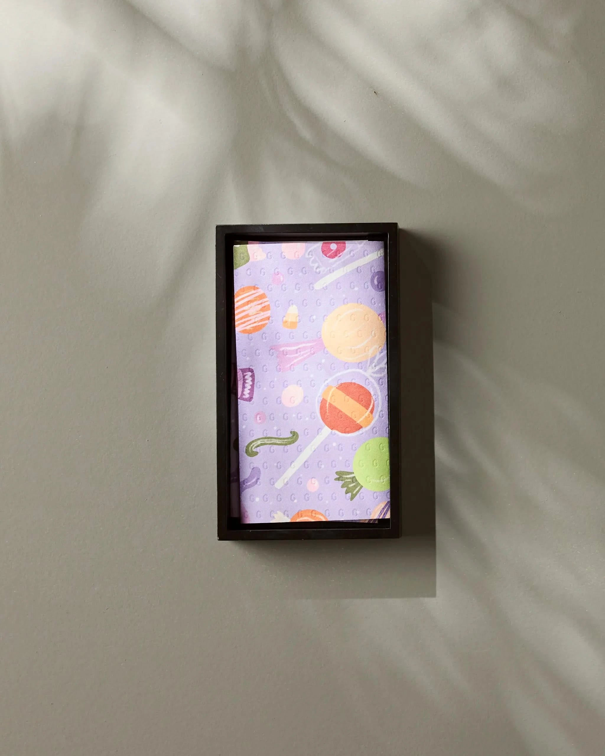 The Geometry Sweet Treasures kitchen towel, featuring colorful planet and space designs, is folded in a small rectangular box on a light gray wall. Soft shadows highlight this eco-friendly and stylish addition to your home.