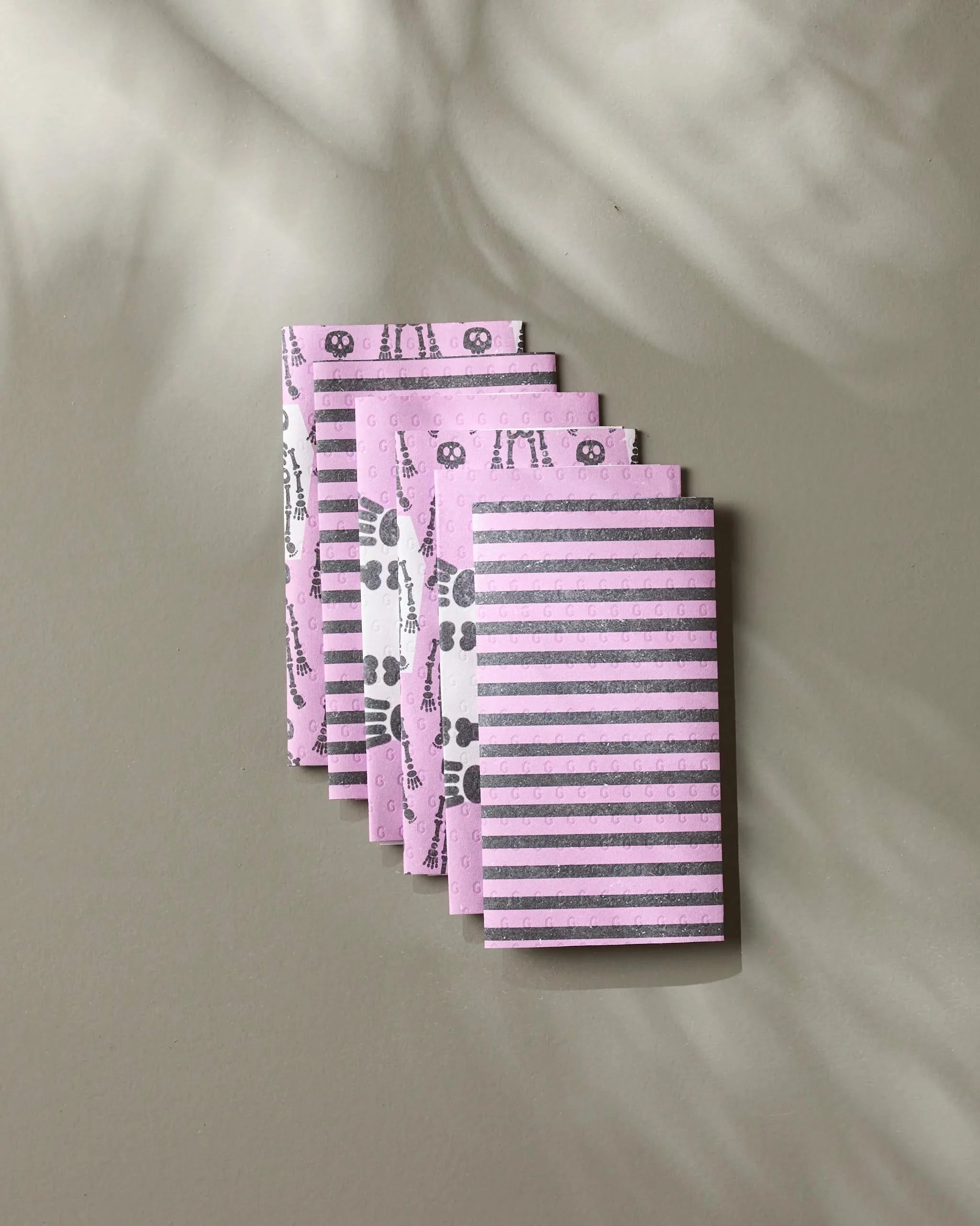 Five small Bright Bones notebooks by Geometry, featuring pink and gray floral, geometric, and striped patterns, are fanned out on a neutral surface—perfect for jotting notes alongside your eco-friendly paper towels.